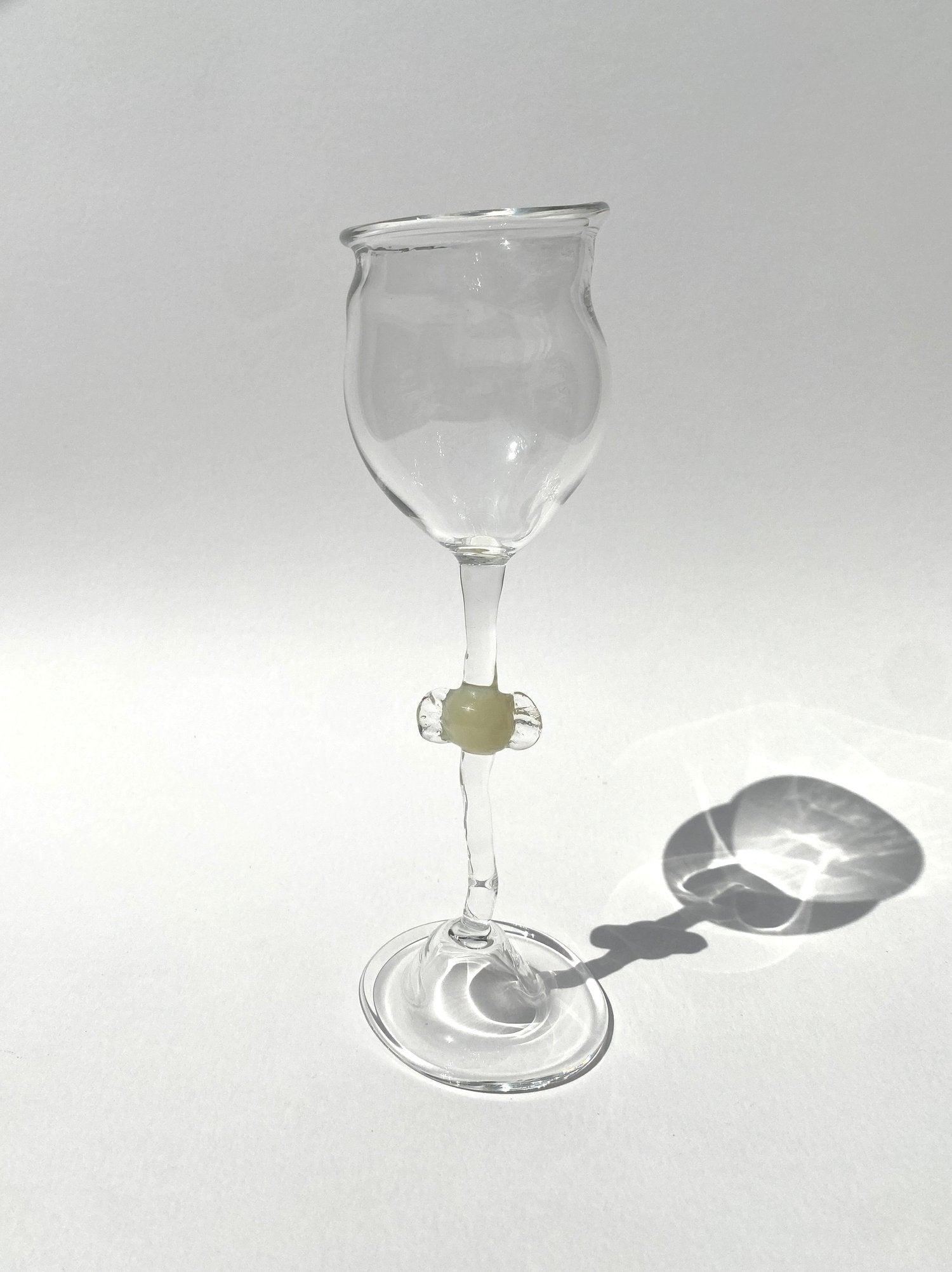 A clear mouth-blown wine glasses by Vivian Alarcón with an ivory candy-shaped embellishment on the stem, displayed against a light background.
