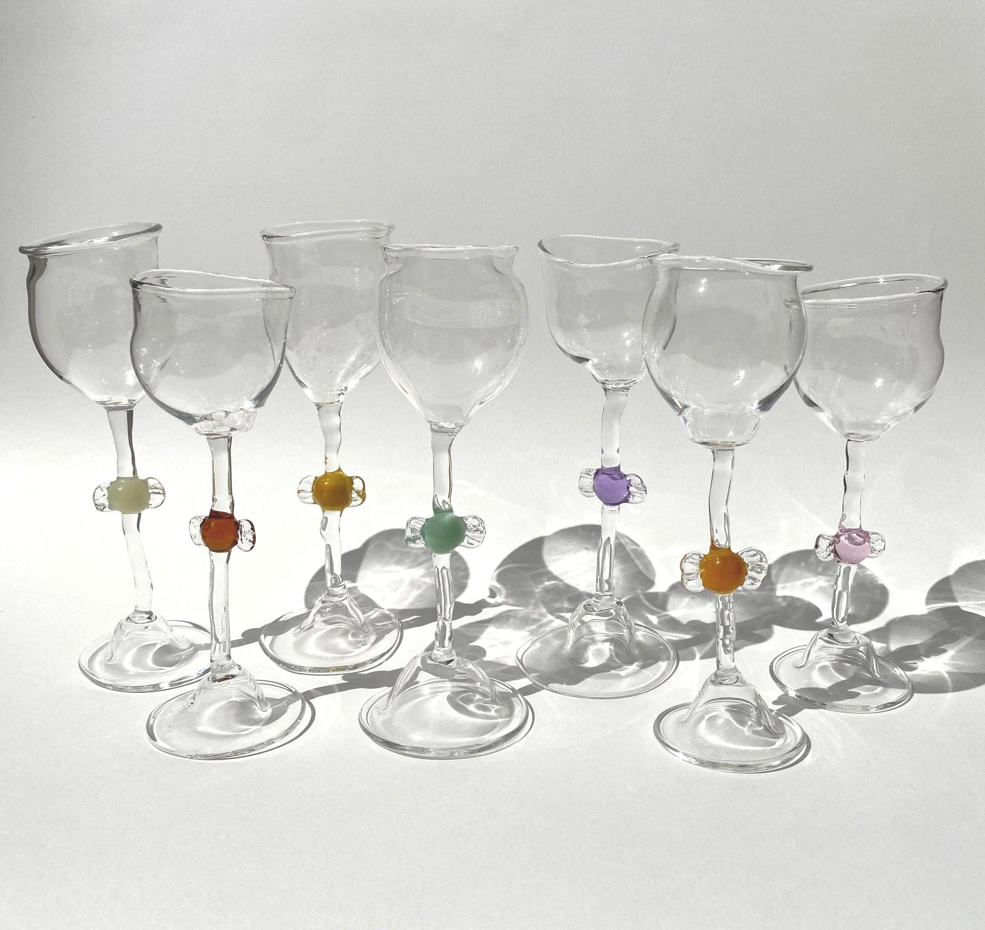 A set of clear mouth-blown wine glasses by Vivian Alarcón with colourful candy-shaped embellishments on the stems, displayed against a light background.