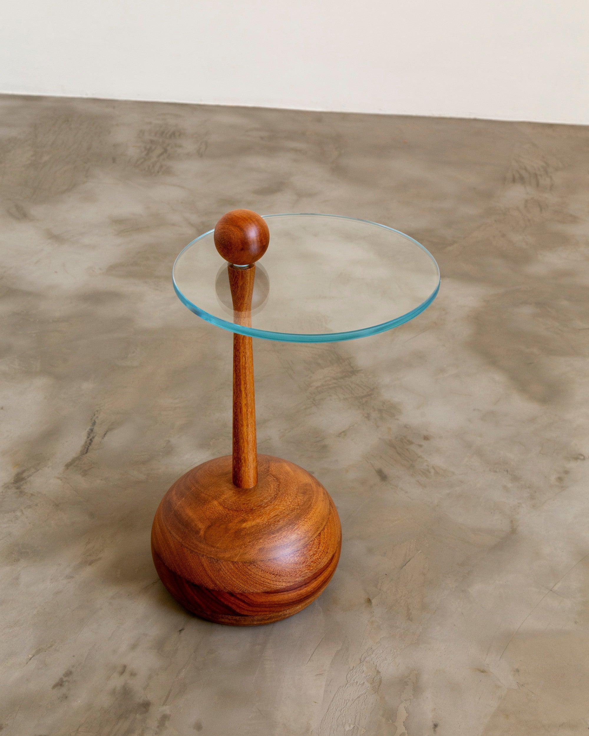 Small round table with wooden base and glass top on a concrete floor by Estudio Prosa.