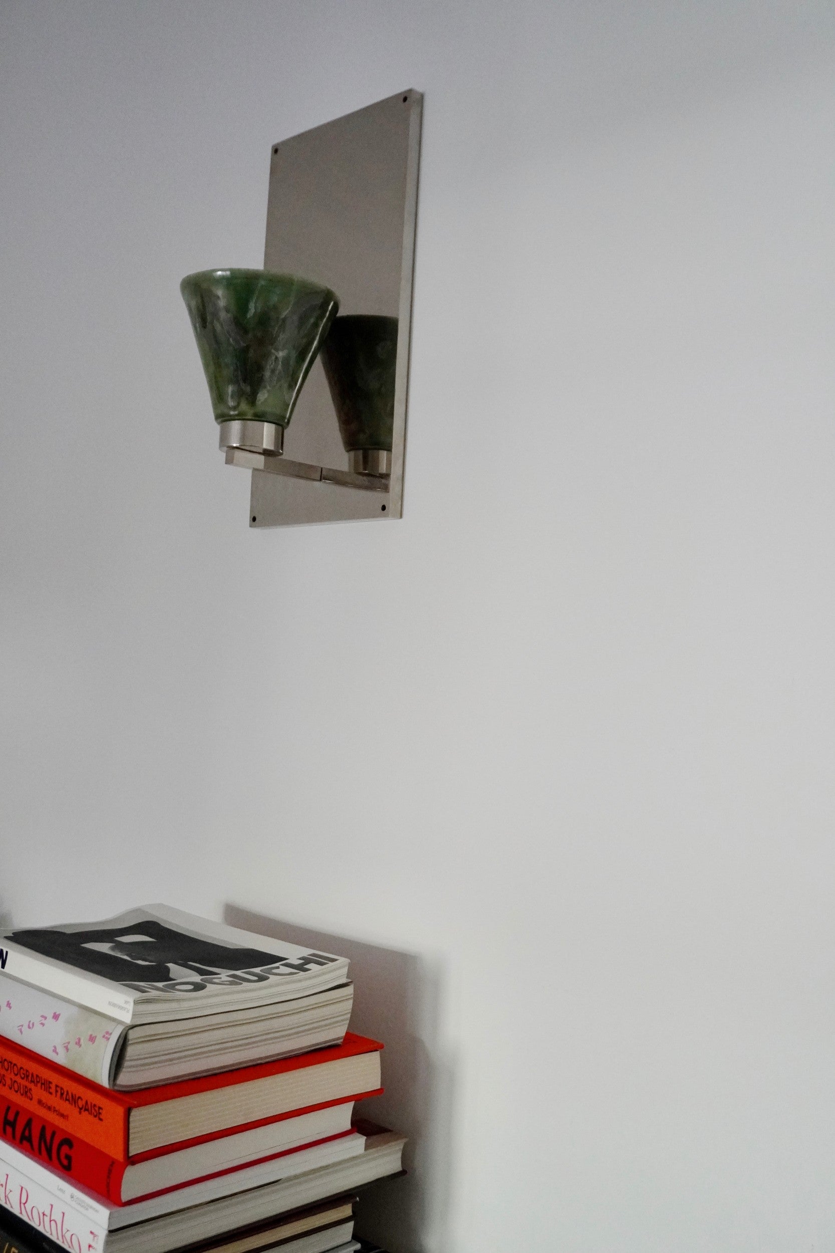 Vetra Lamp by Marta Cypel, mounted on a white wall above a stack of books.