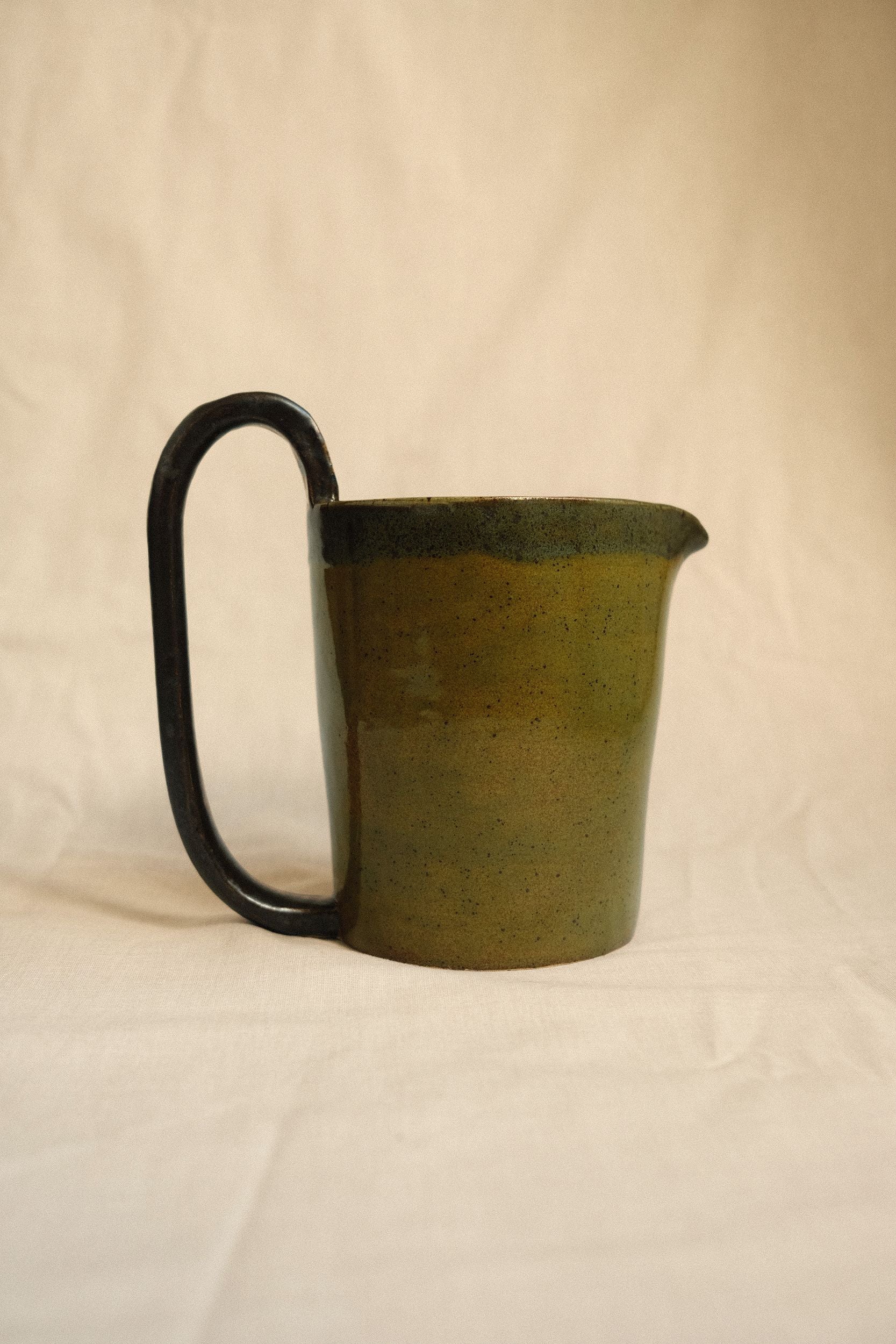Green ceramic pitcher with an oversized handle by Bira Ceramics on a beige background.