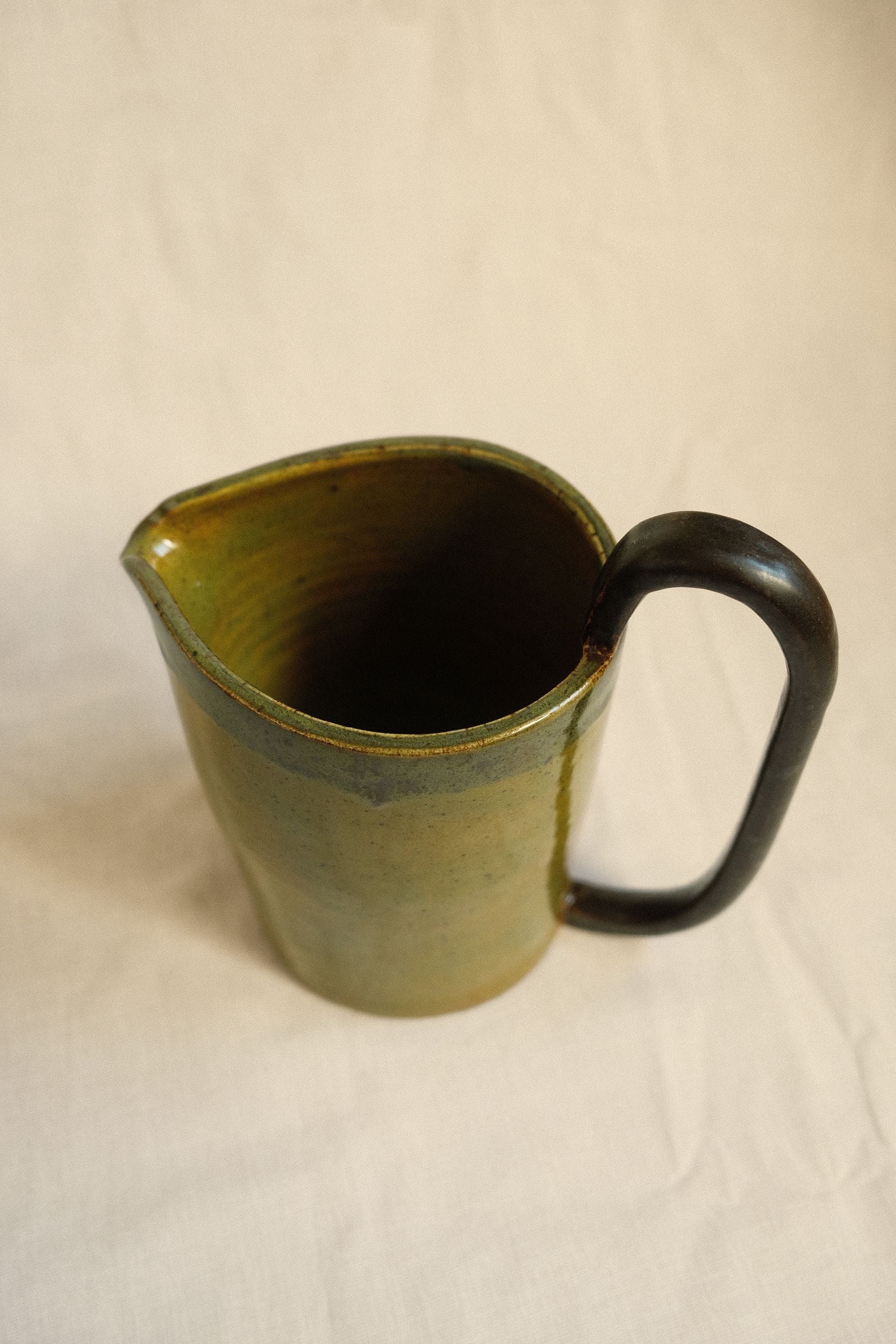 Green ceramic pitcher with an oversized handle by Bira Ceramics on a beige background.