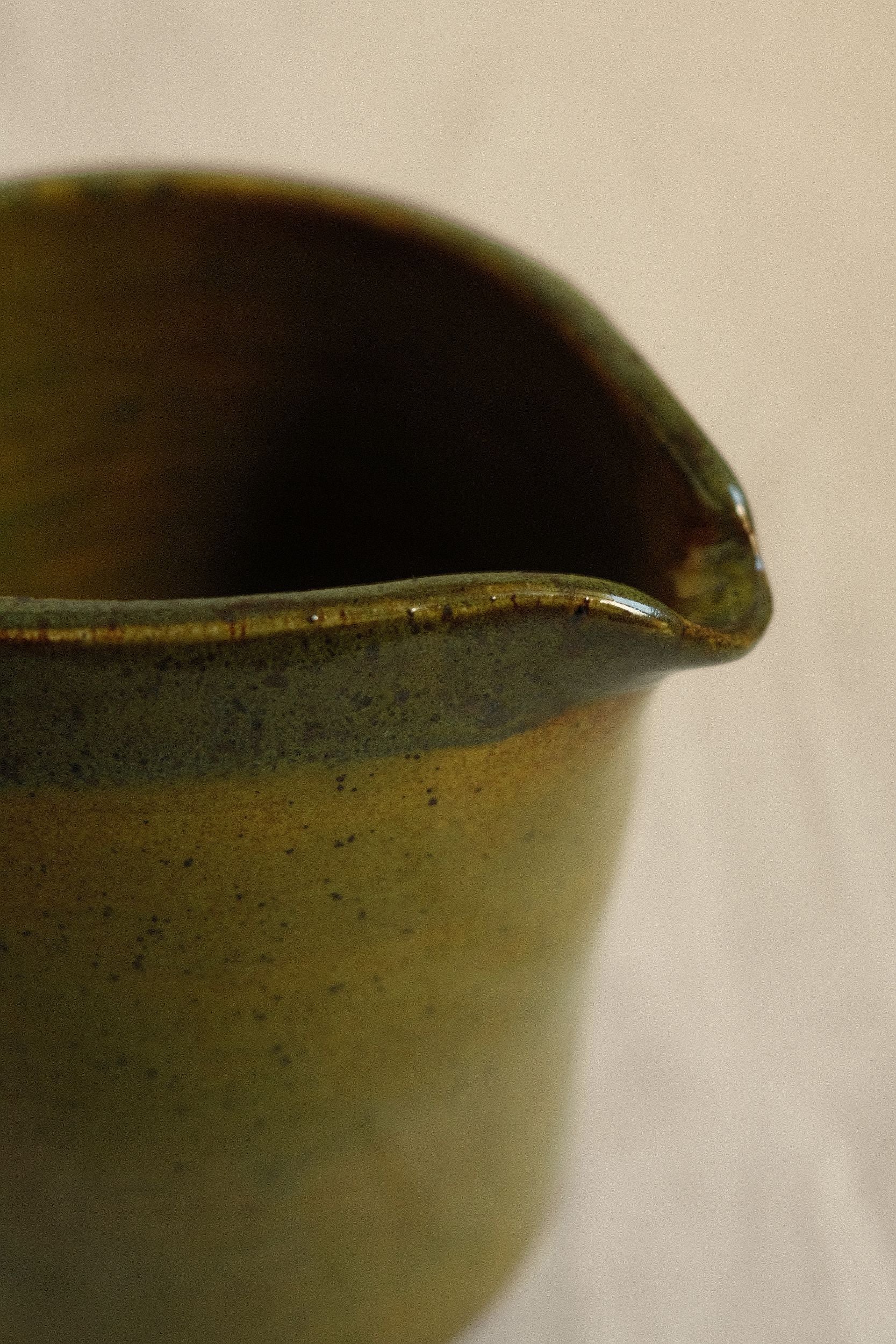 Close up of green ceramic pitcher spout by Bira Ceramics on a blurred beige background.