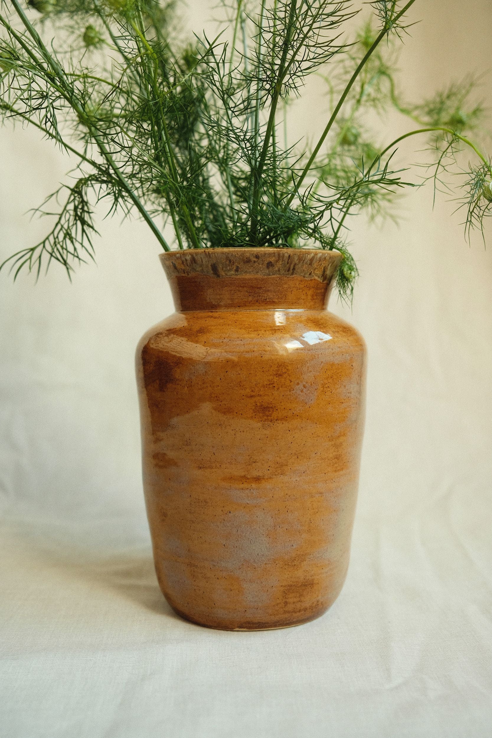 Ochre glazed ceramic vase by Bira Ceramics with green flowers on a beige background.