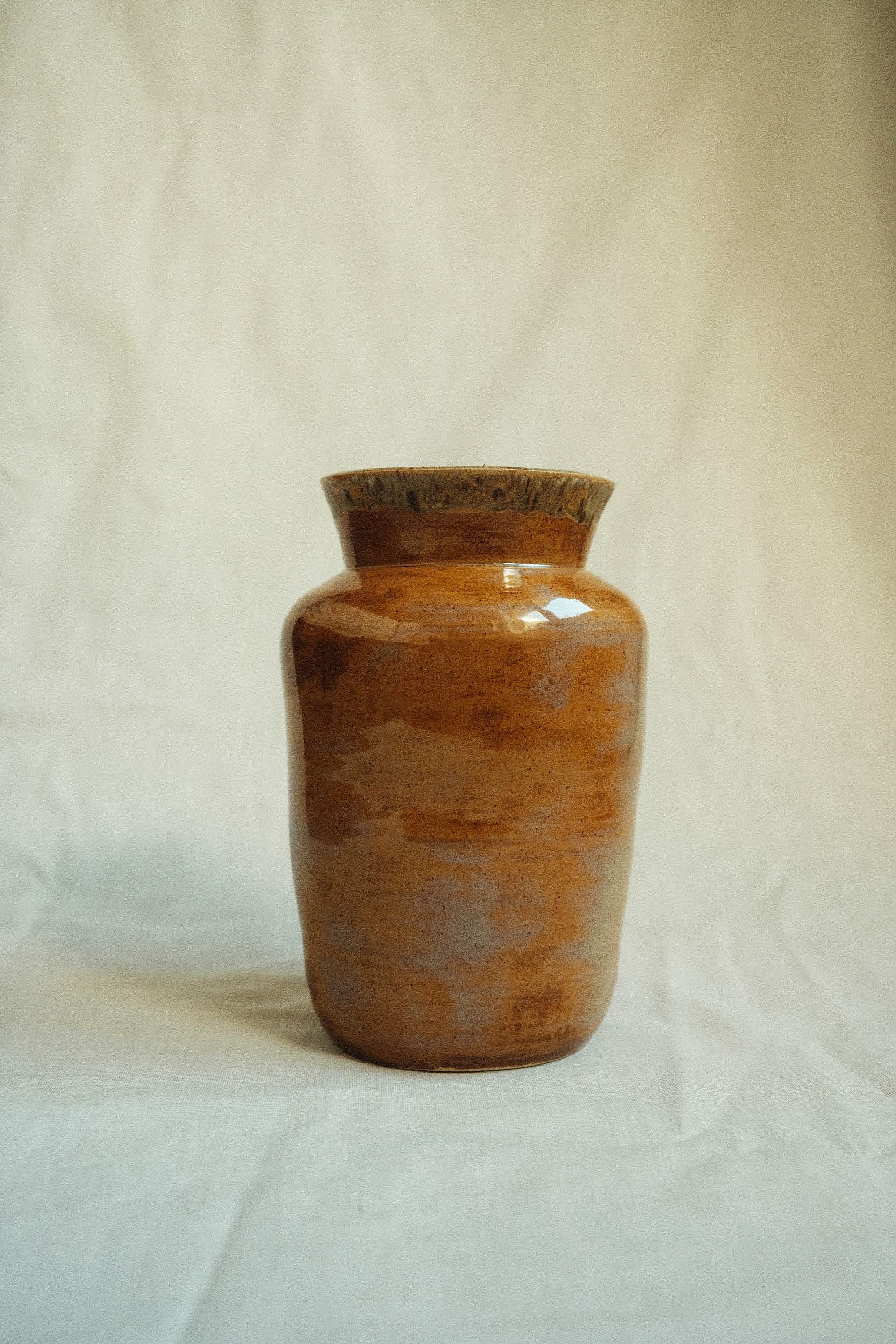 Ochre glazed ceramic vase by Bira Ceramics on a beige background.