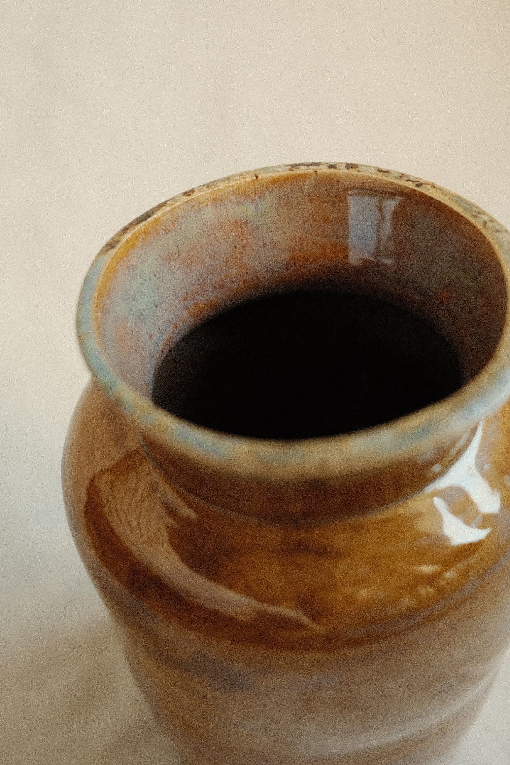 Close up of ochre glazed ceramic vase by Bira Ceramics on a beige background.