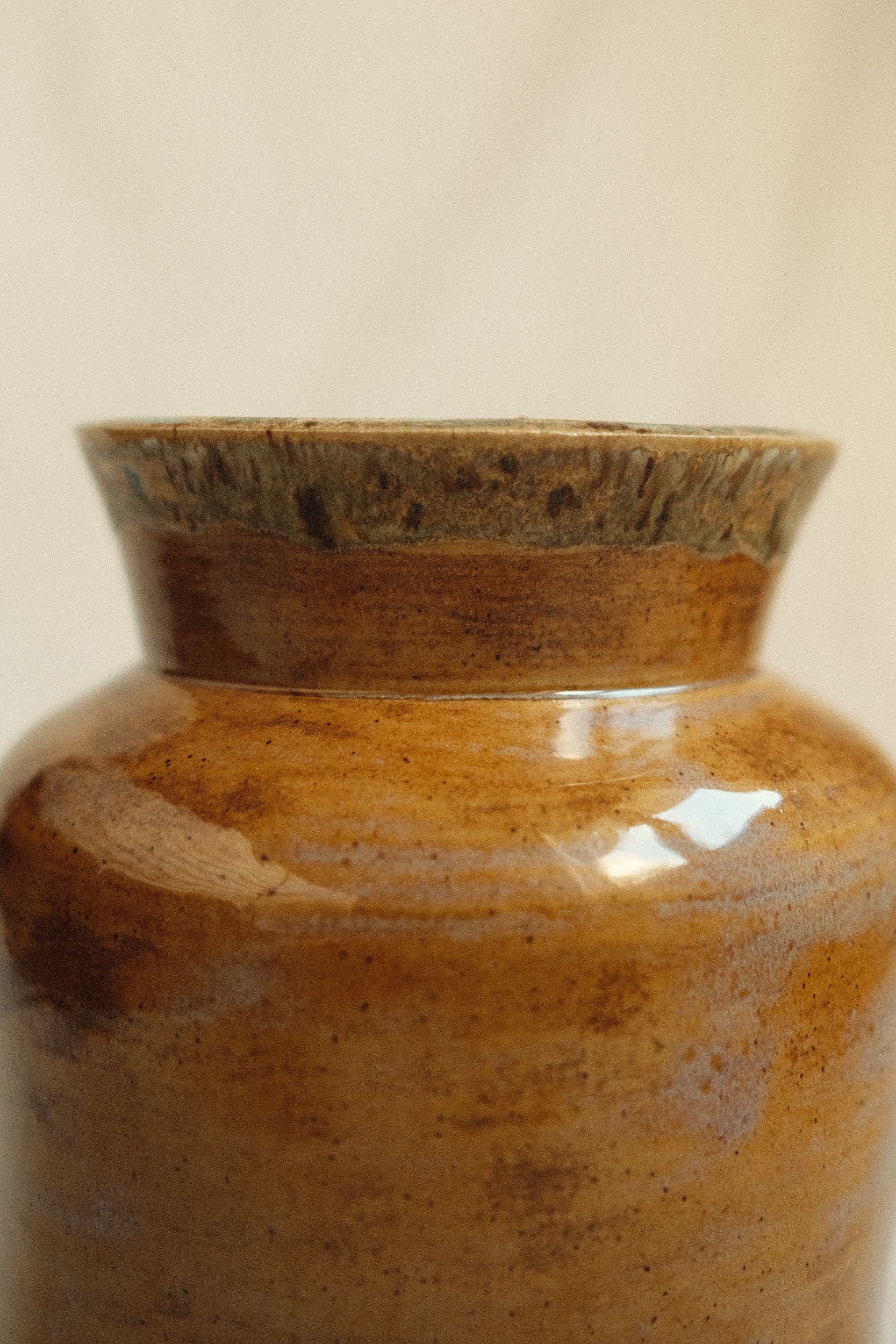 Close up of ochre glazed ceramic vase by Bira Ceramics on a beige background.