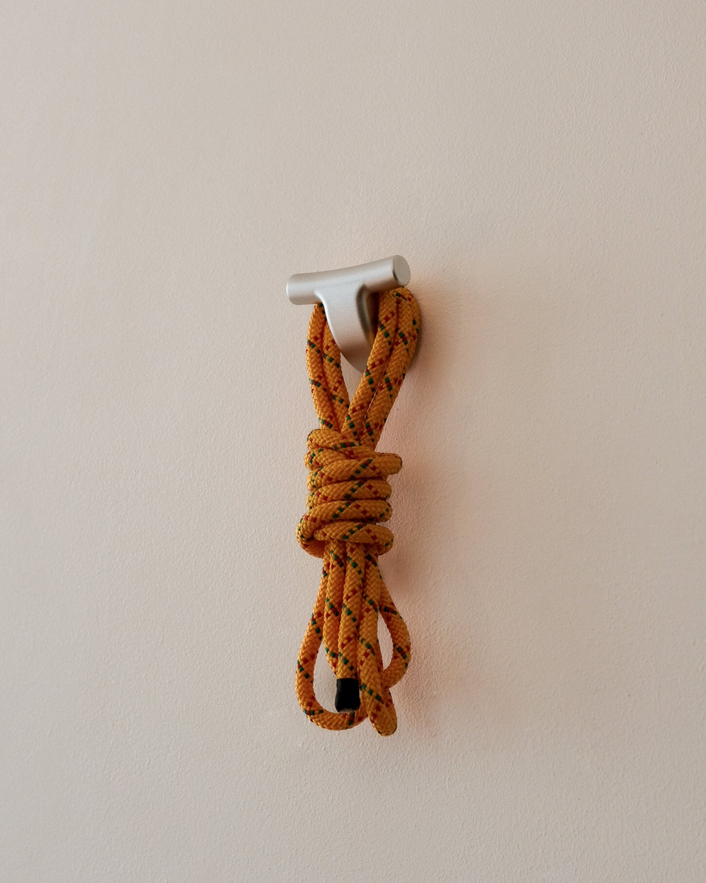 Silver mooring hook by PARCTA mounted on a neutral wall with rope hooked around it.