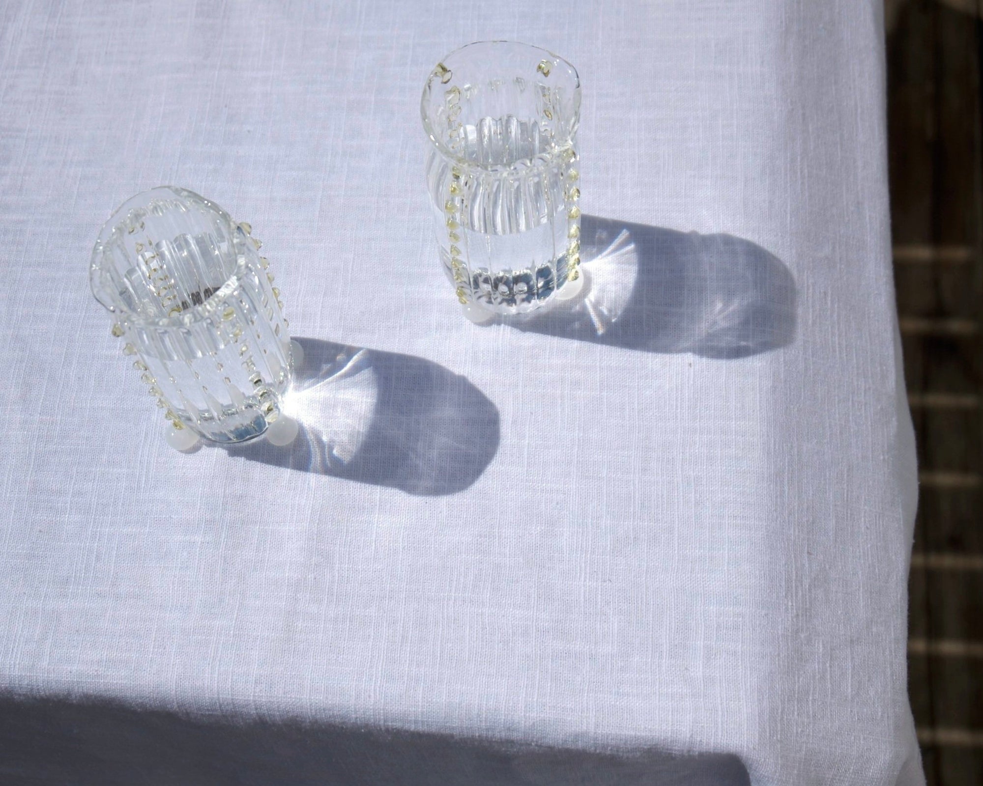 Two mouth-blown, decorative water glasses by Vivian Alarcón on a table with white table linen.