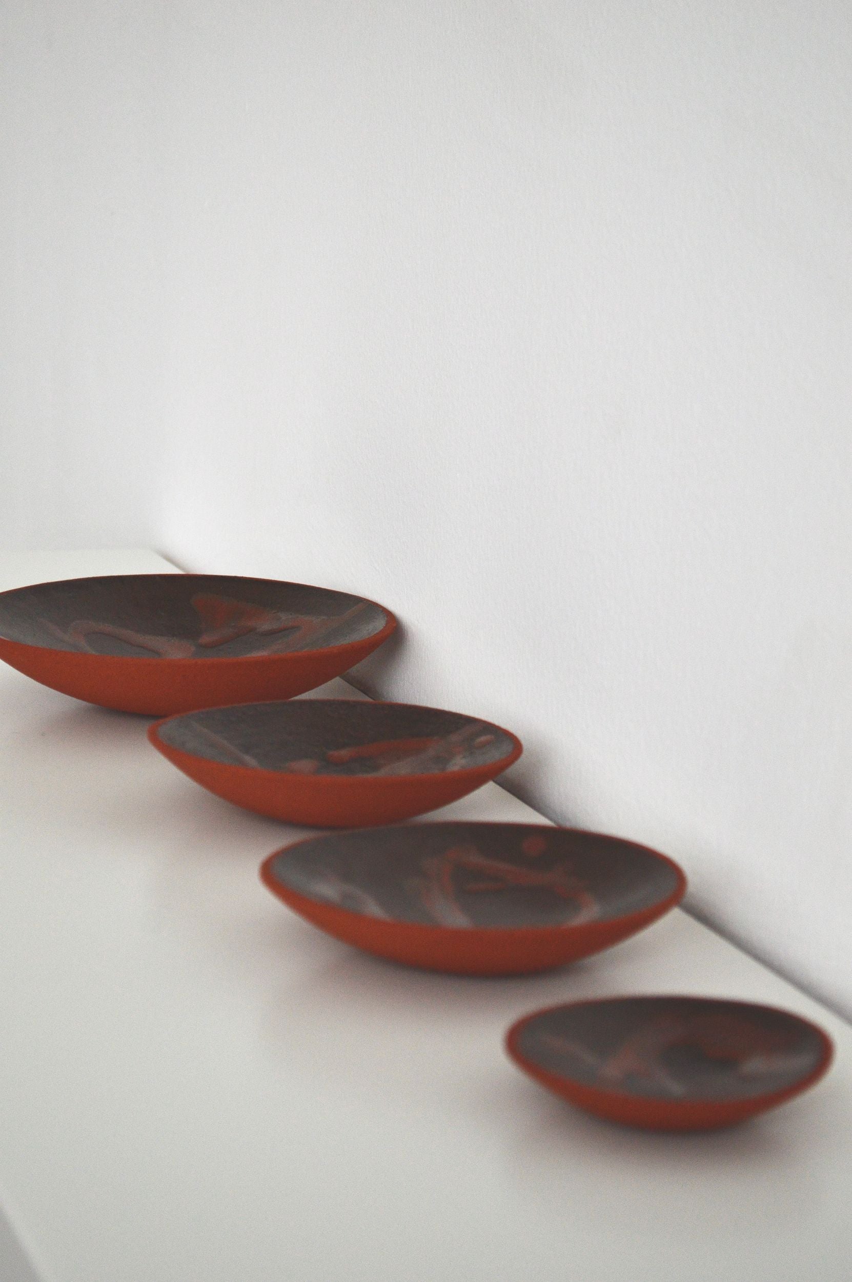 A set of four decorative ceramic plates with an organic swirling pattern in shades of brown by Zeynep Boyan. The plates are positioned besides each other to show the different size variations.