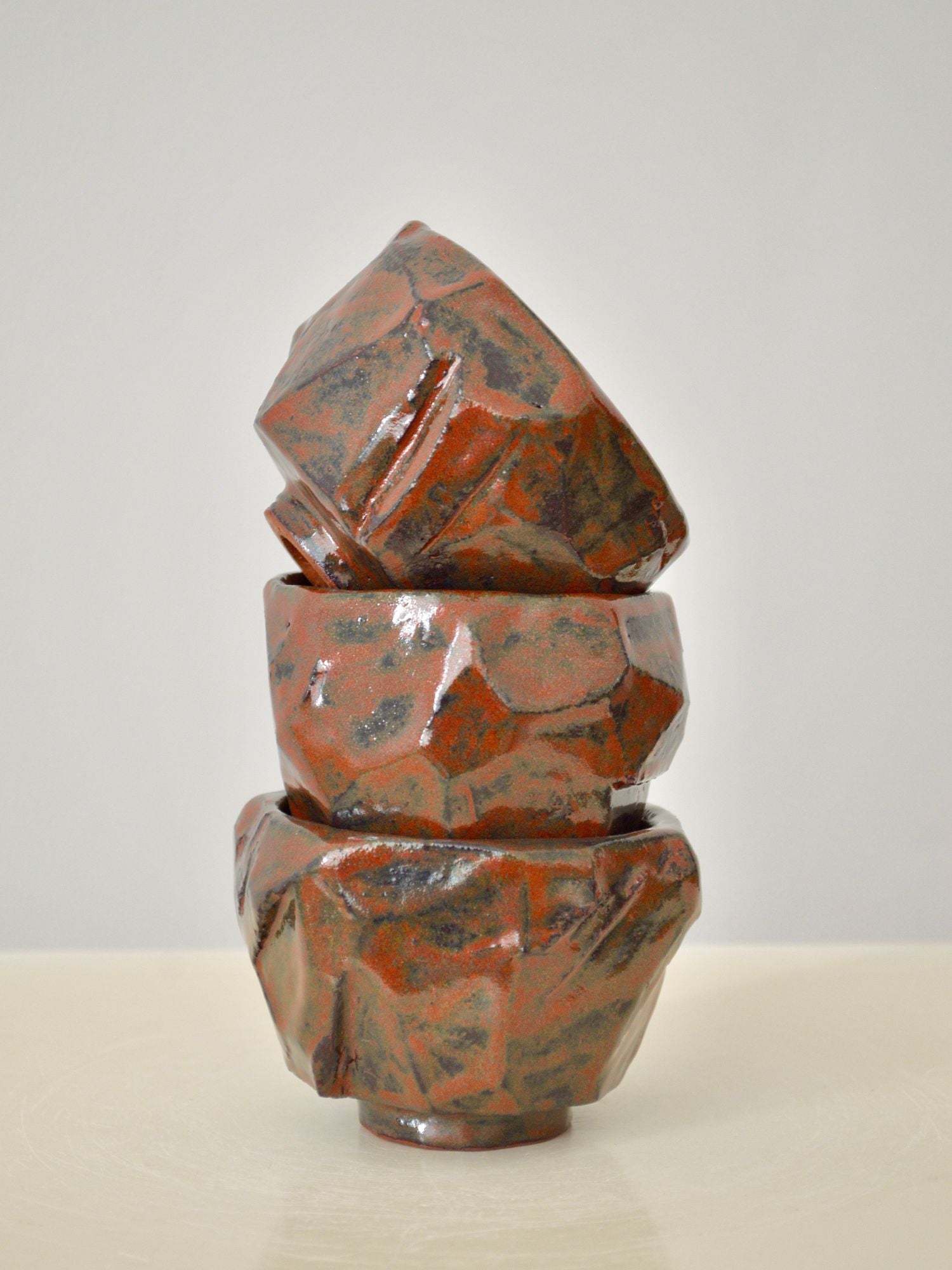 A stack of three ruby coloured coffee cups by Zeynep Boyan on a neutral background.