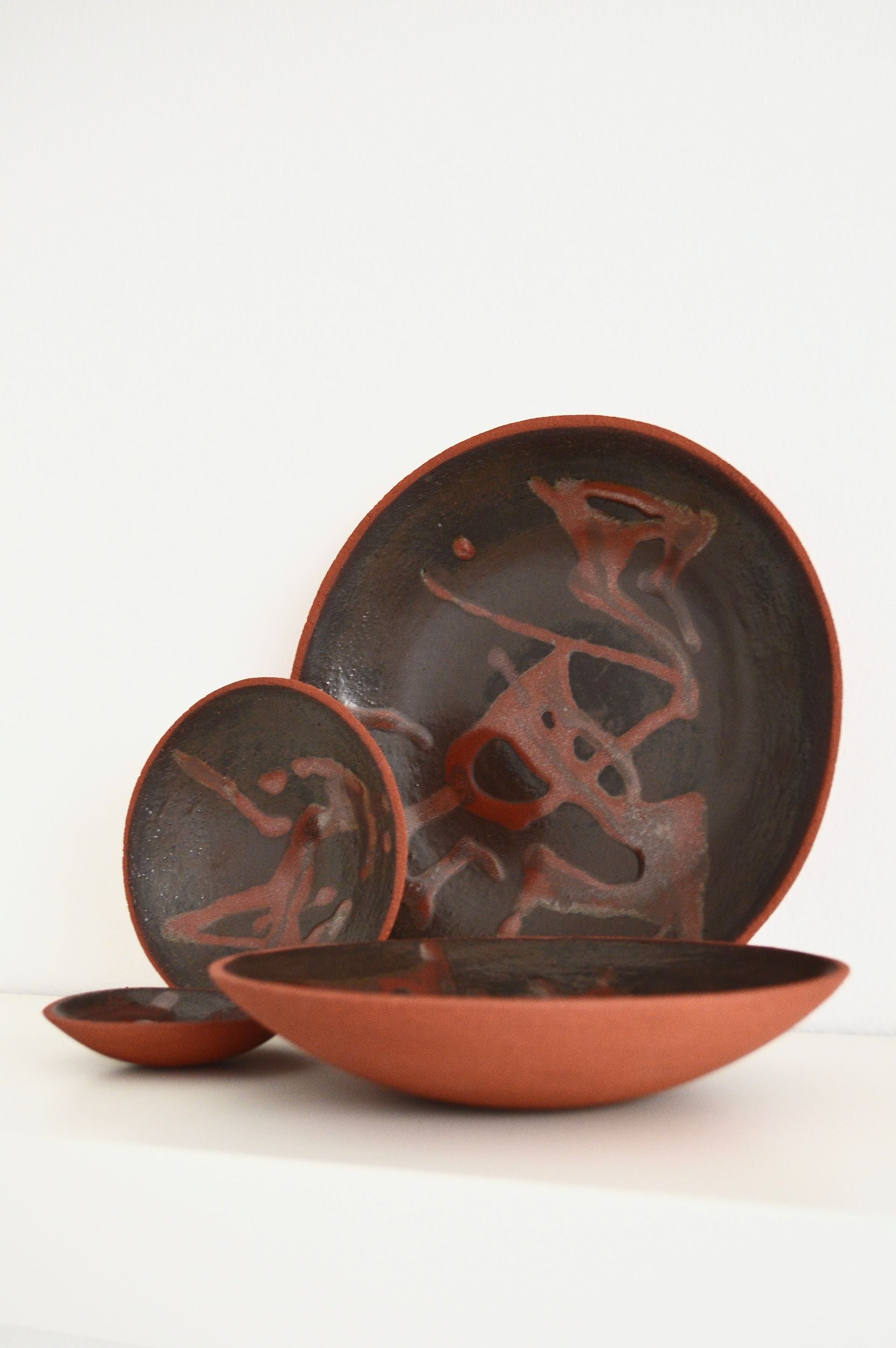 A set of decorative ceramic plates with an organic swirling pattern in shades of brown by Zeynep Boyan. The plates are positioned besides each other. 