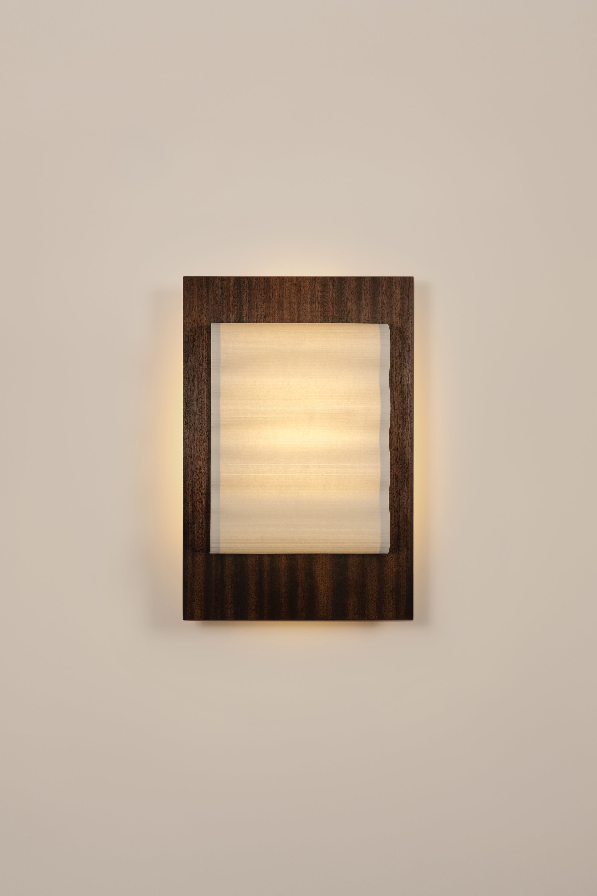 Framed wall light fixture in wood with a paper shade by Violaine d'Harcourt on a beige wall with light on.