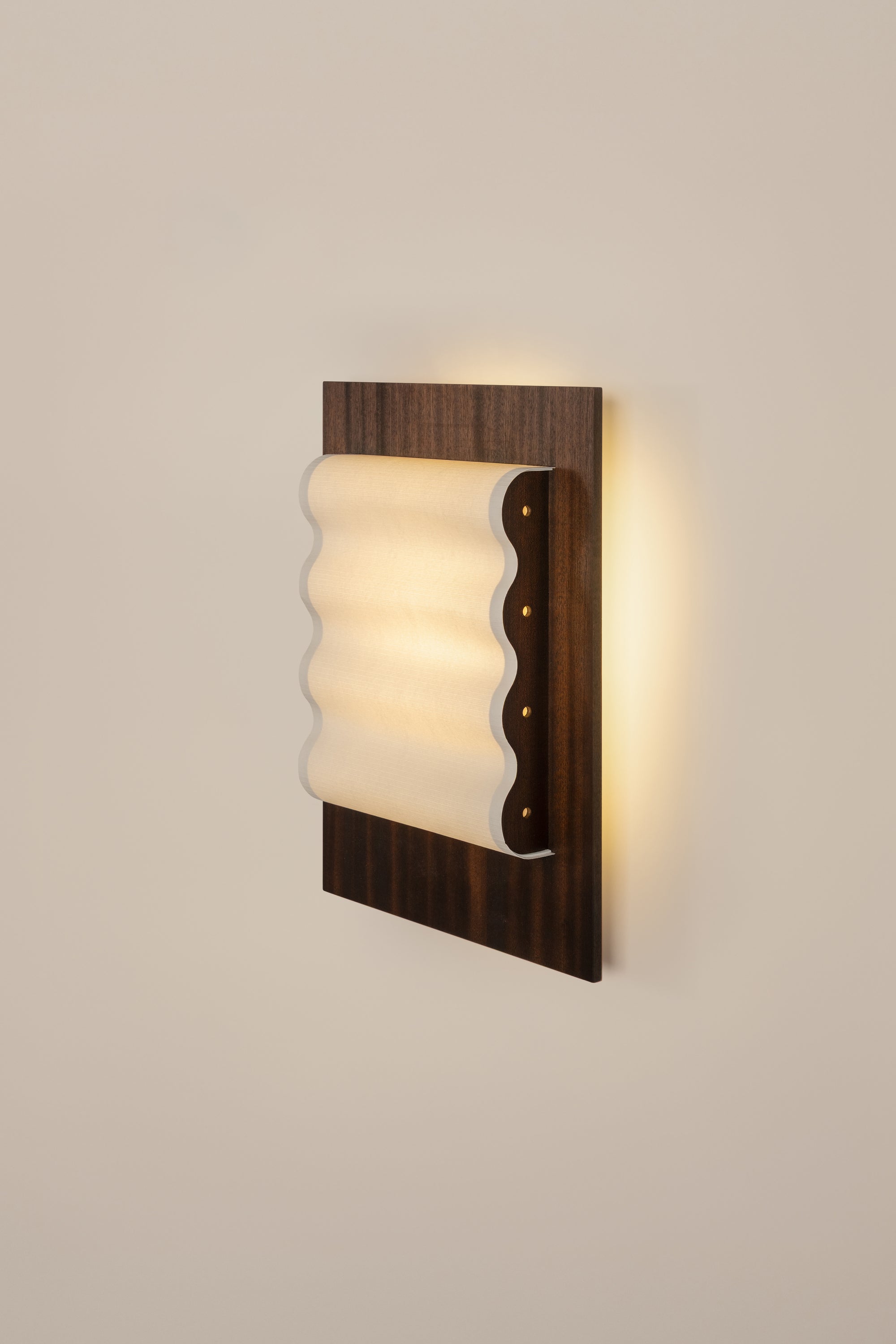 Framed wall light fixture in wood with a paper shade by Violaine d'Harcourt on a beige wall with light on.