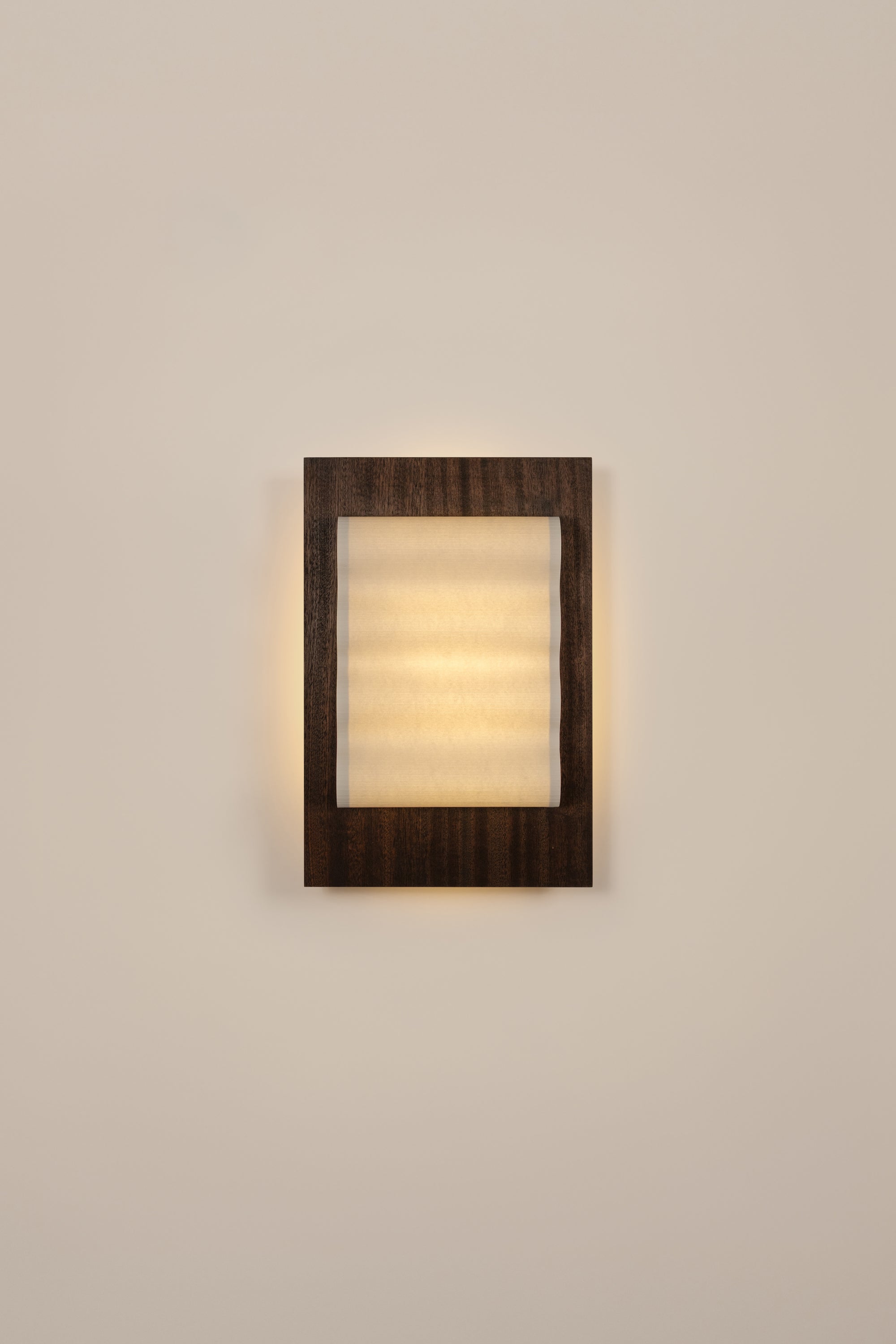 Framed wall light fixture in wood with a paper shade by Violaine d'Harcourt on a beige wall with light on.
