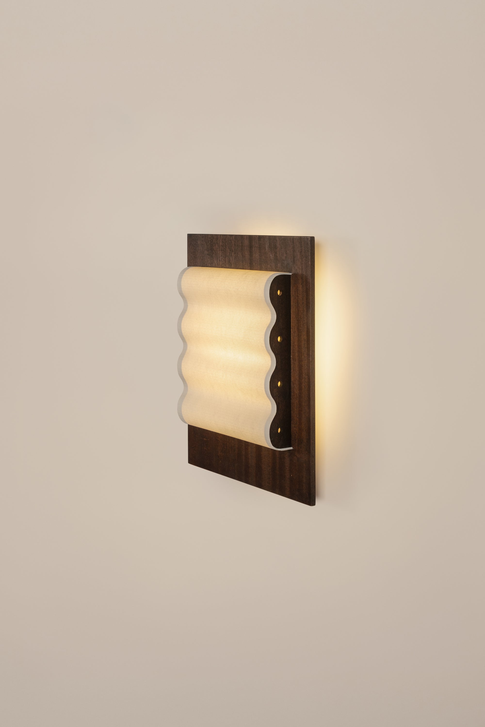 Framed wall light fixture in wood with a paper shade by Violaine d'Harcourt on a beige wall with light on.
