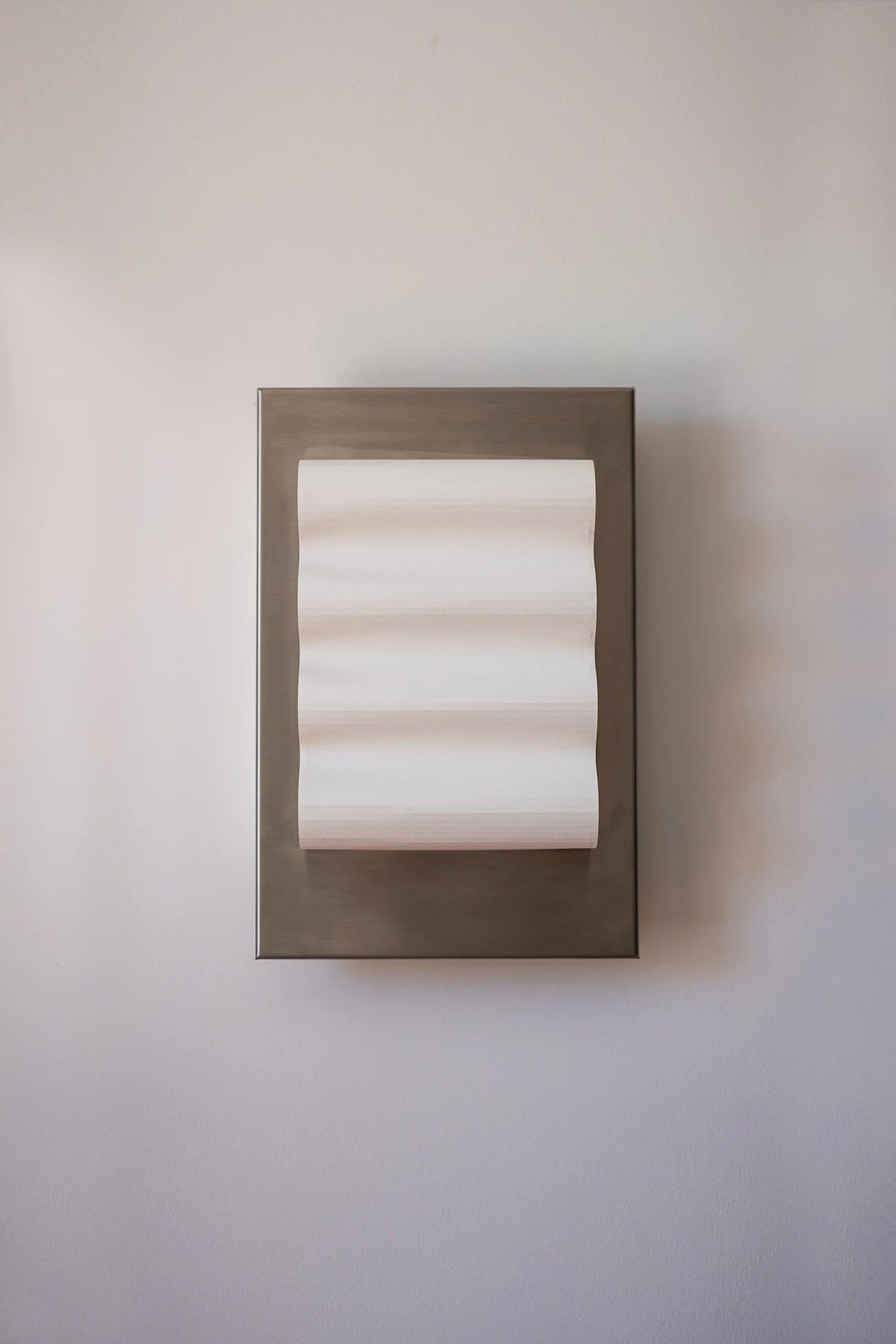 Framed wall light fixture in raw stainless steel with a paper shade by Violaine d'Harcourt on a beige wall with light off.