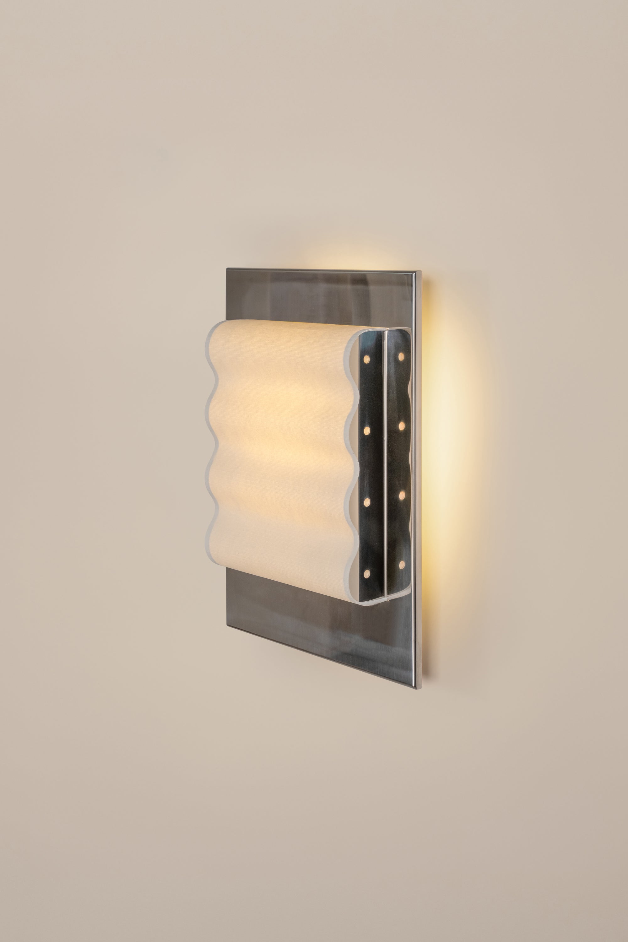 Framed wall light fixture in polished stainless steel with a paper shade by Violaine d'Harcourt on a beige wall with light on.