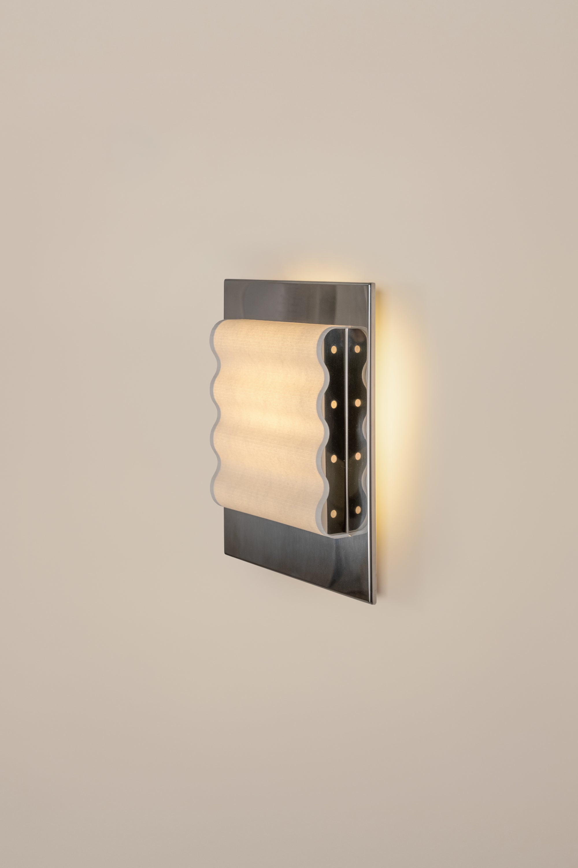 Framed wall light fixture in polished stainless steel with a paper shade by Violaine d'Harcourt on a beige wall with light on.