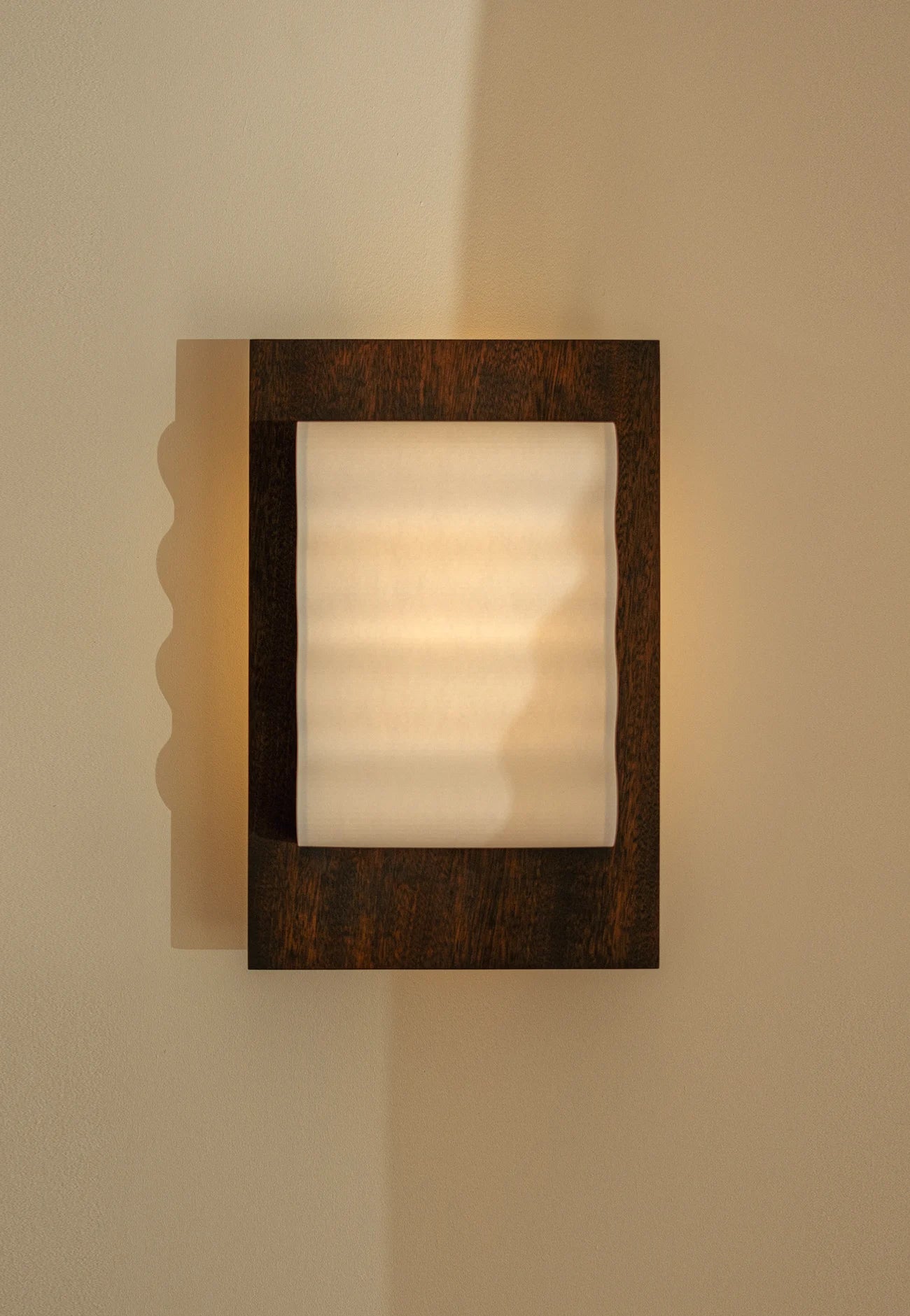 Framed wall light fixture in wood with a paper shade by Violaine d'Harcourt on a beige wall with light off.