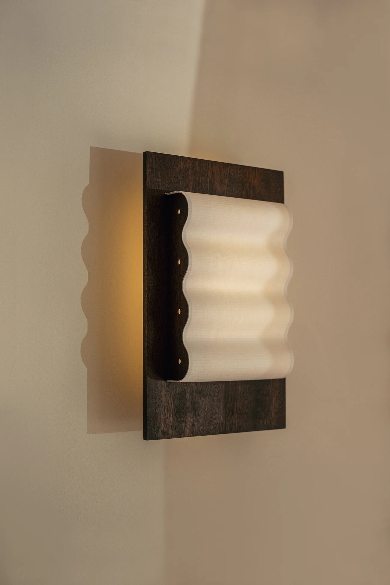 Framed wall light fixture in wood with a paper shade by Violaine d'Harcourt on a beige wall with light on.