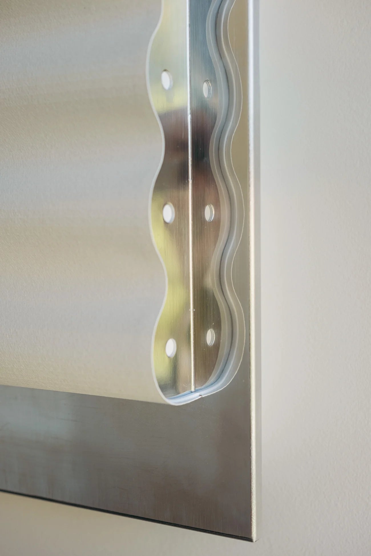 Close up of framed wall light fixture in polished stainless steel with a paper shade by Violaine d'Harcourt on a beige wall with light off.