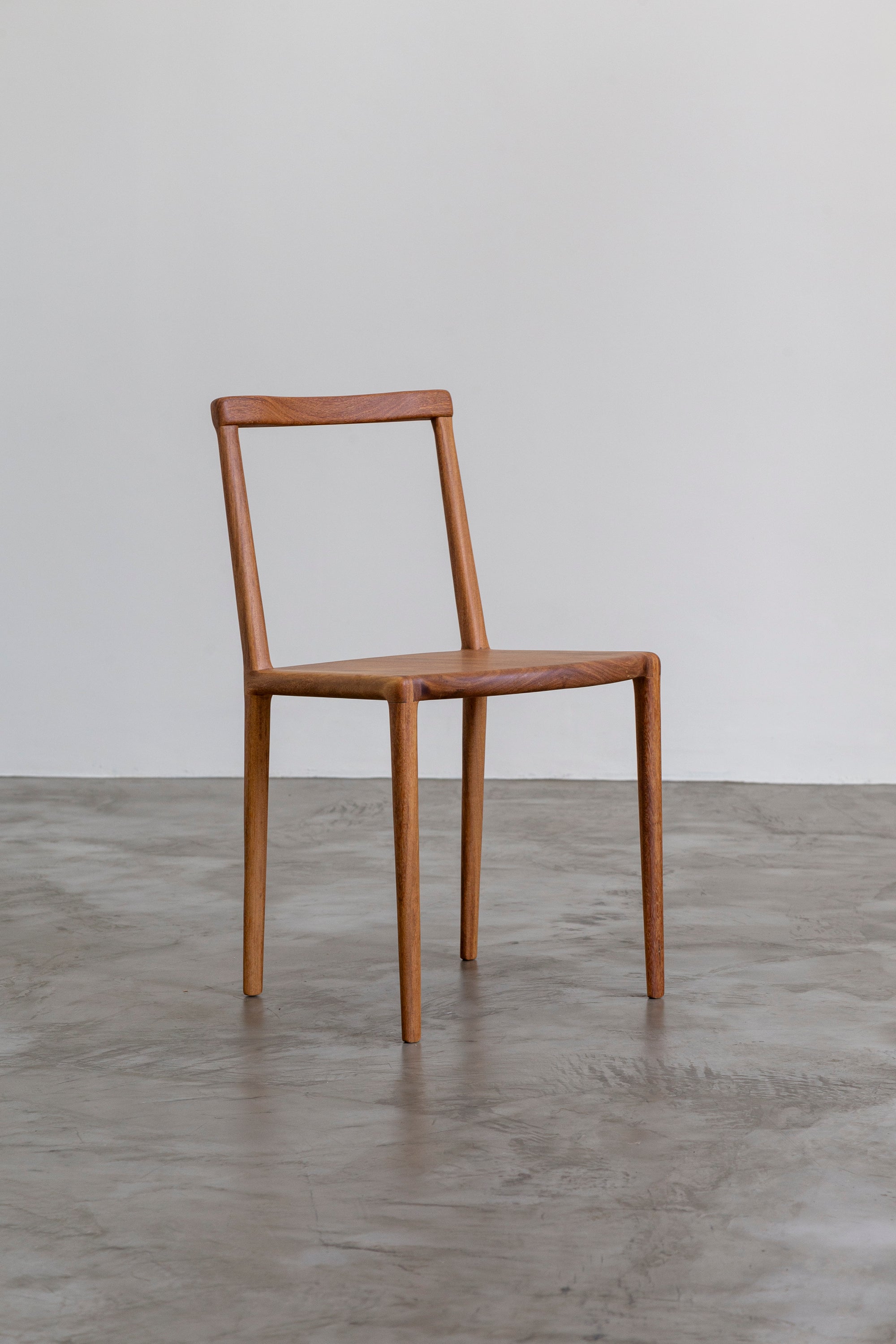 Wooden chair by Estudio Prosa on a grey concrete floor with a white wall background.