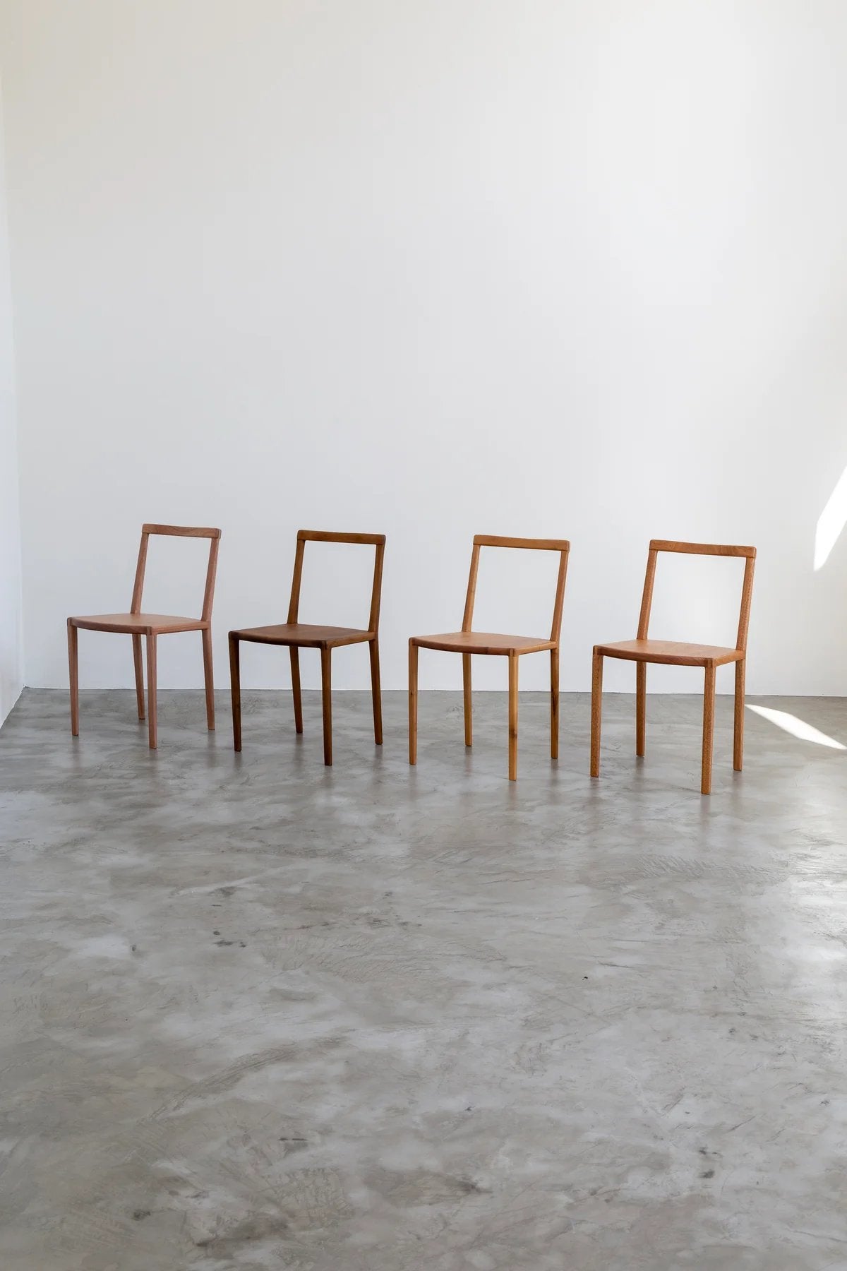 Four wooden chairs by Estudio Prosa against a white background on a grey concrete floor.