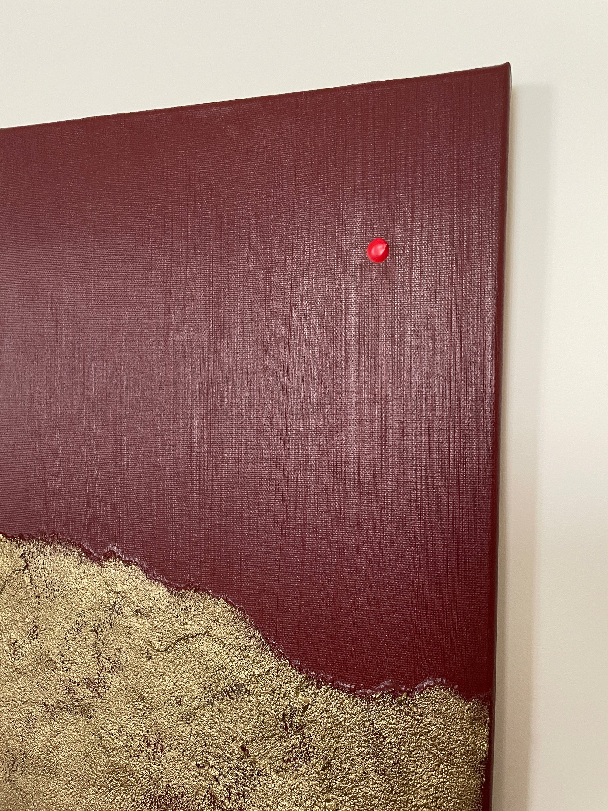 Close up of red and gold abstract art by Noelia Hobeika on a white wall, showing the textures of the painting.