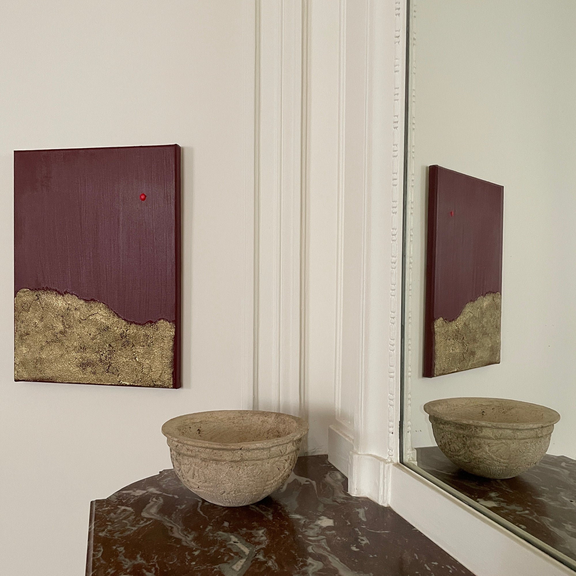 Red and gold abstract wall art by Noelia Hobeika on a white wall, besides a marble fire that has a stone decorative bowl positioned on top.