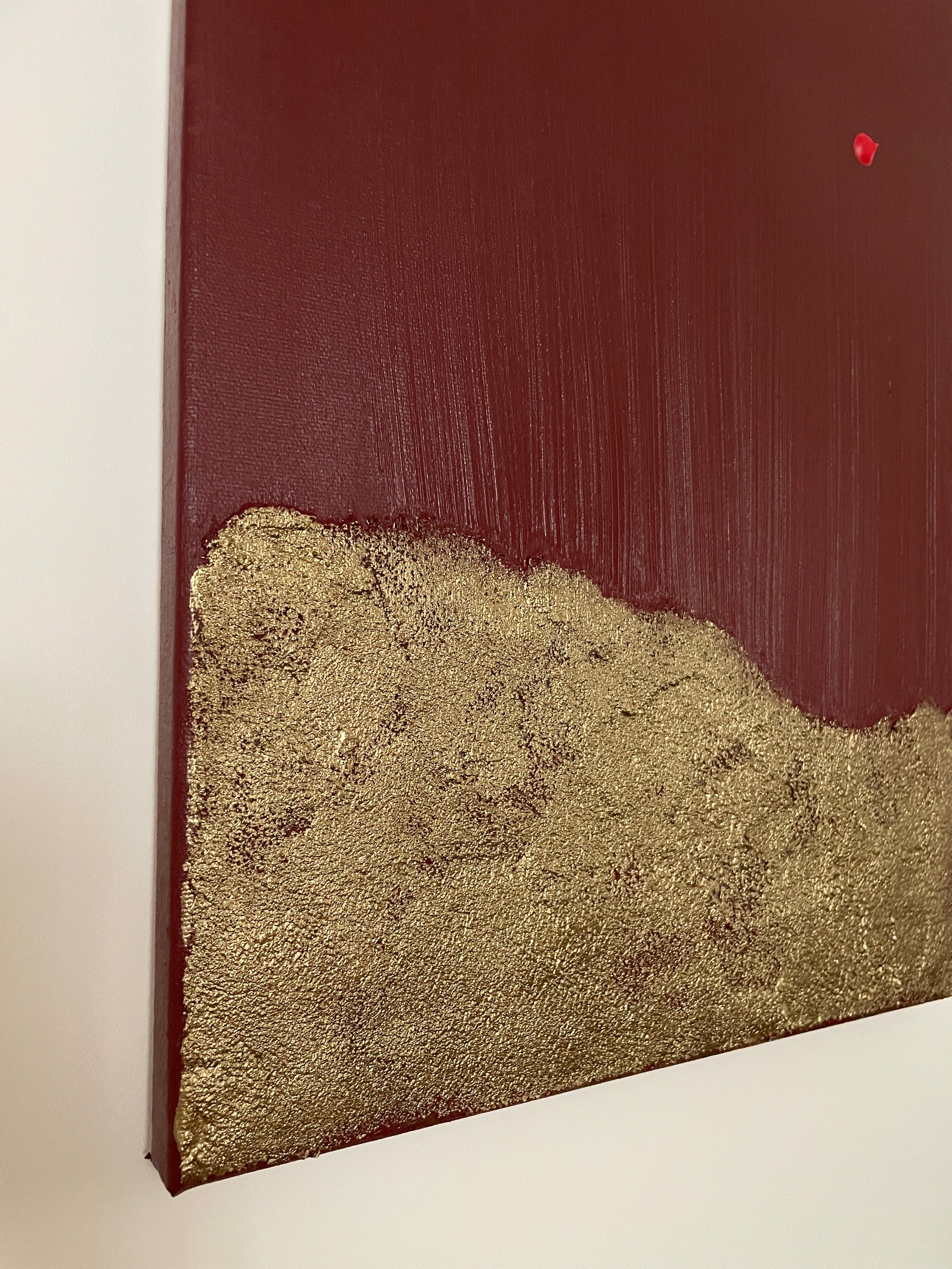 Close up of red and gold abstract art by Noelia Hobeika on a white wall, showing the textures of the painting.