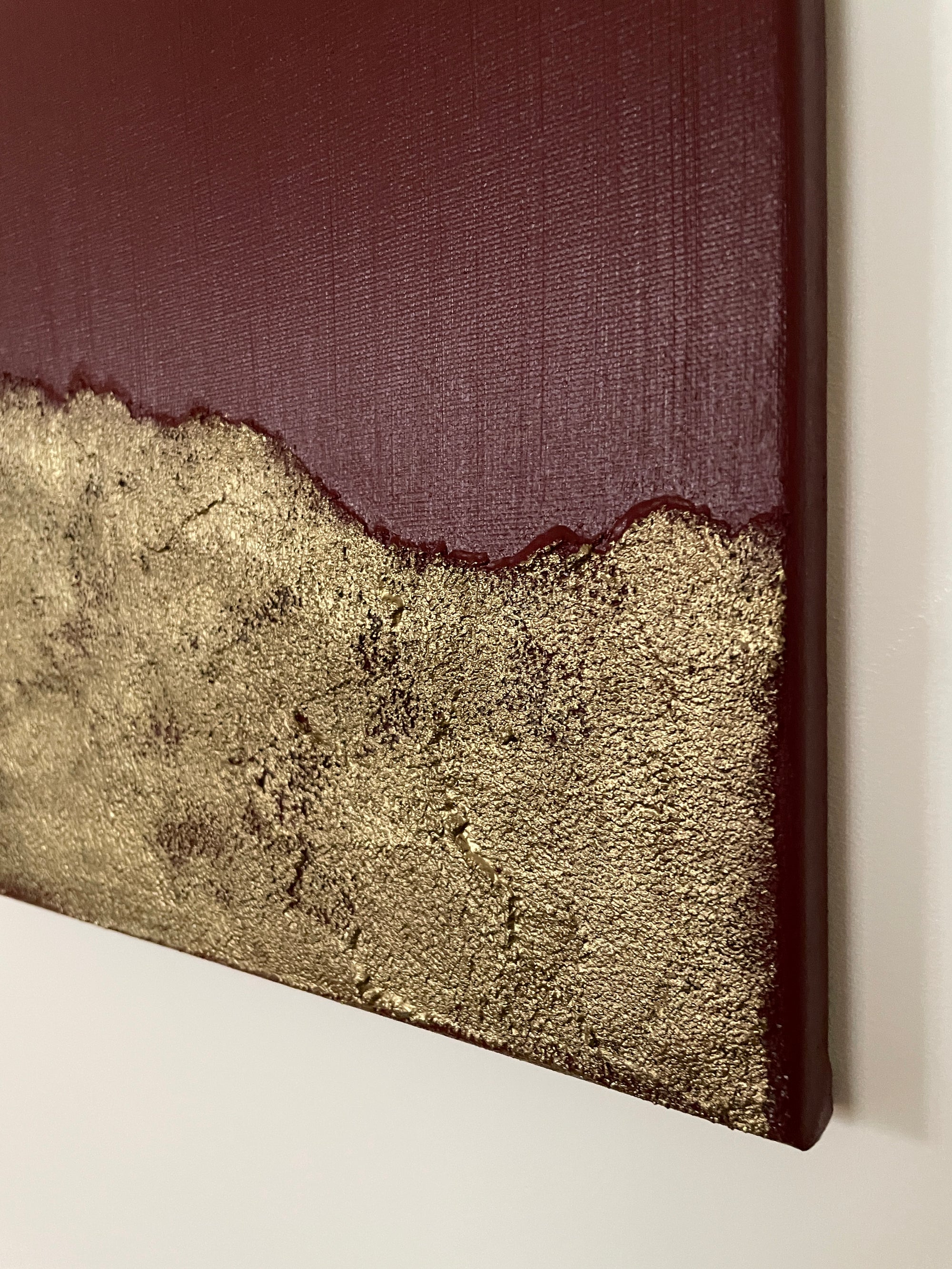 Close up of red and gold abstract art on a white wall by Noelia Hobeika, showing the textures of the painting.