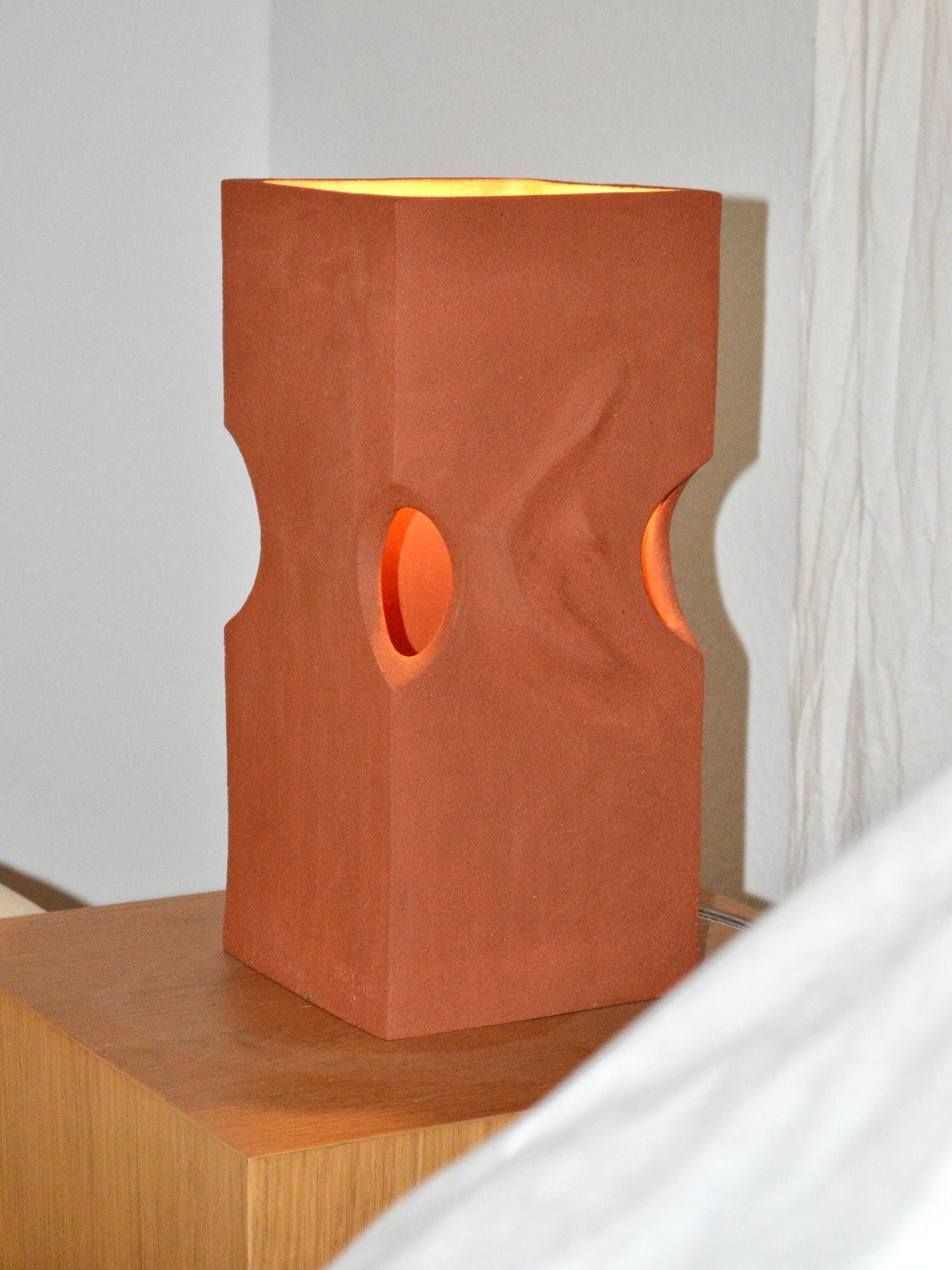 Ceramic lamp by Zeynep Boyan sat on a wooden side table with the light on.