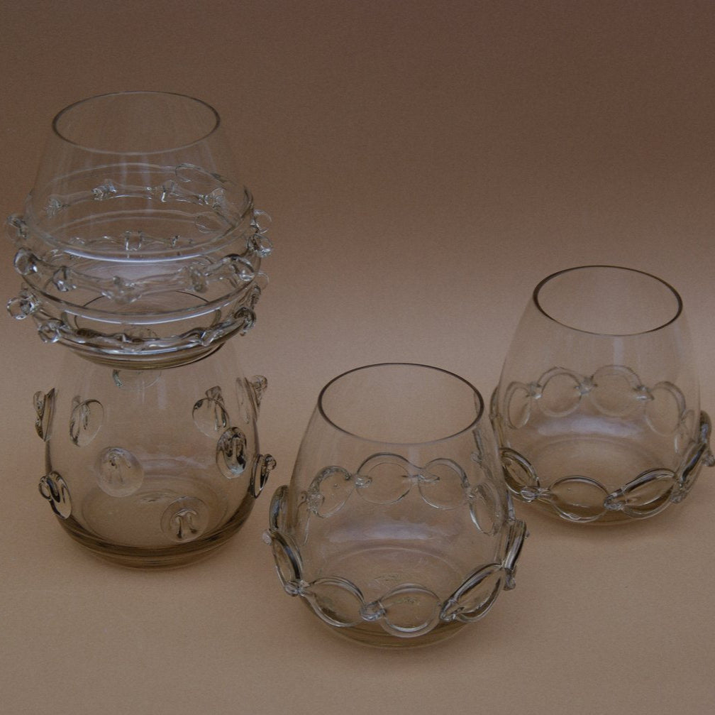 Four smokey grey water glasses with glass decorative accents by Lucie Claudia on a beige background.

