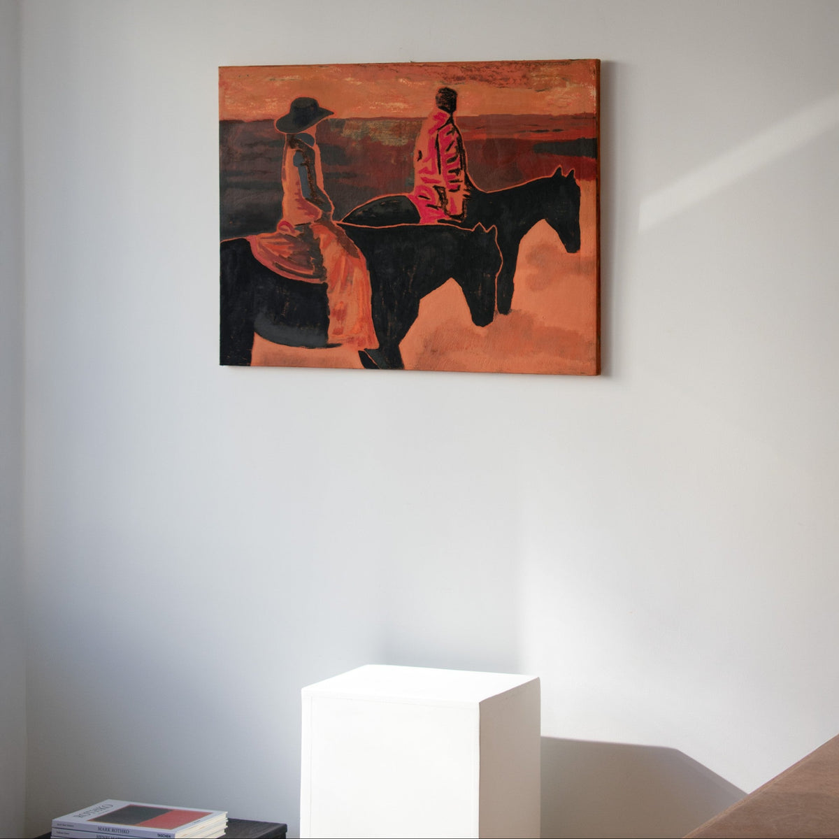An original painting by Marcsen, depicting two riders on horseback in warm orange, red, black, and brown tones, displayed on a neutral wall above a white pedestal.
