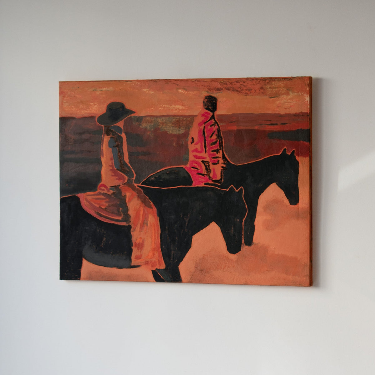 An original painting by Marcsen hanging on a white wall, depicting two riders on horseback in warm orange, red, black, and brown tones.