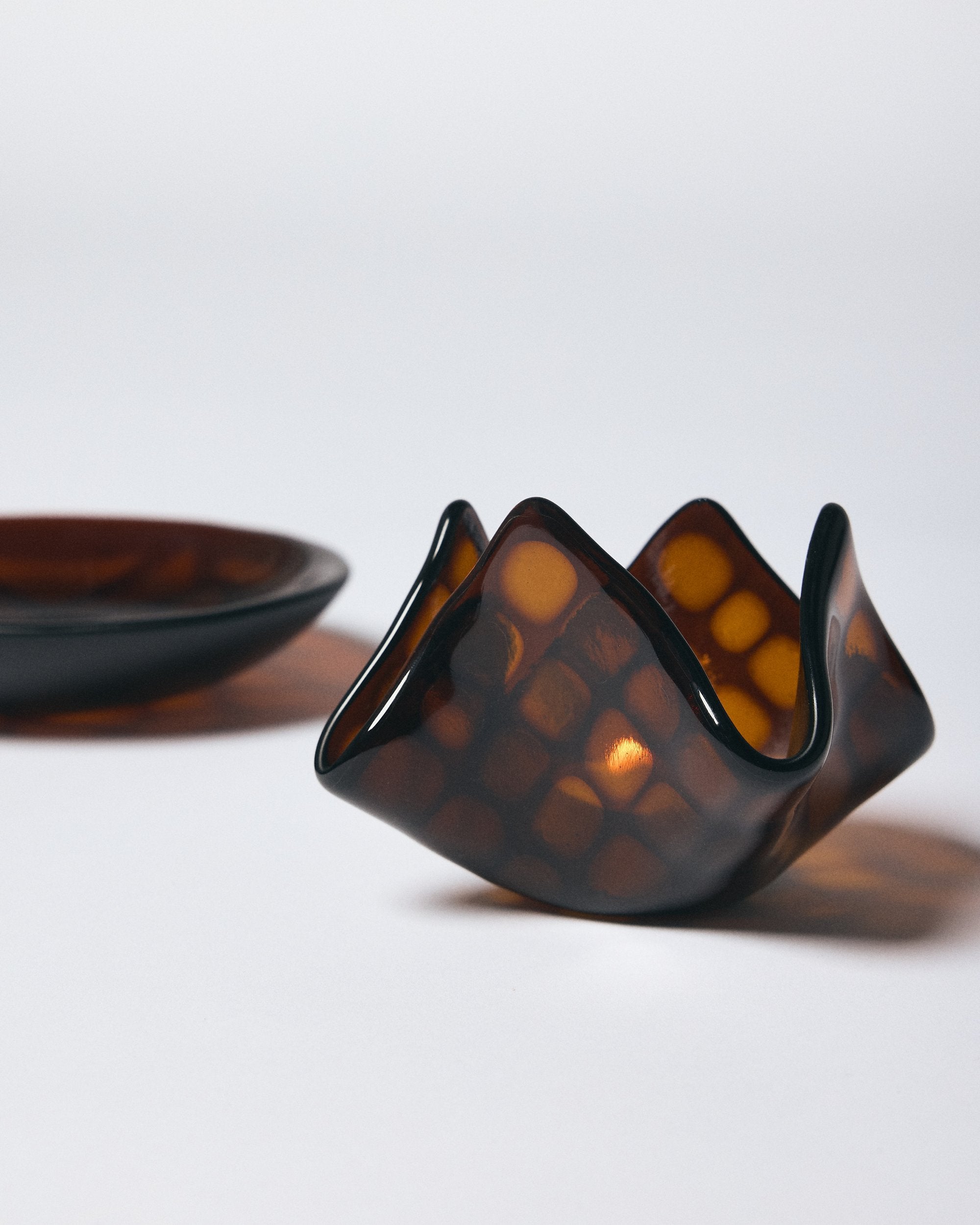 Dark amber patterned glass candle holder with candle lit inside and matching glass bowl by Savoia Everything on a white background. 