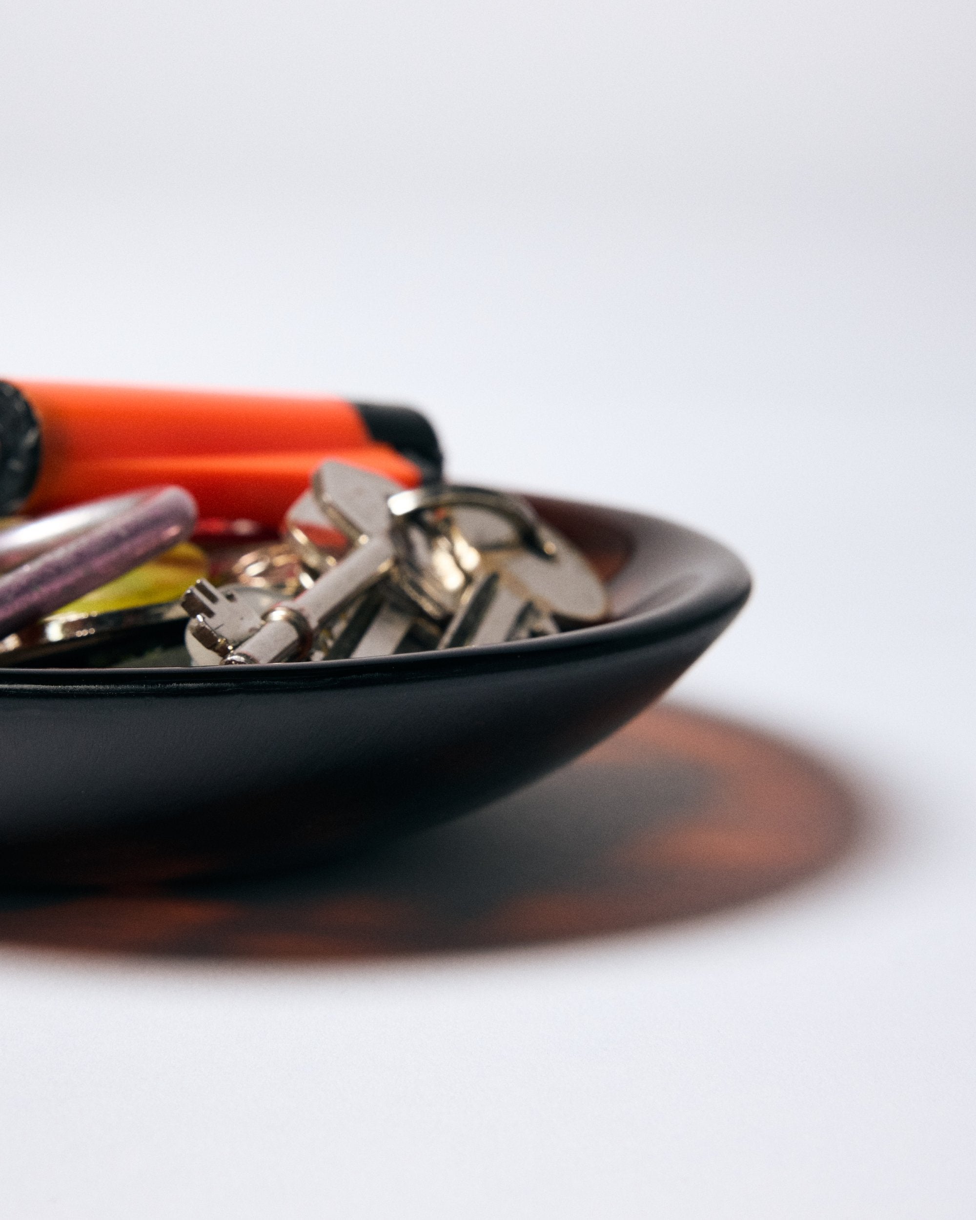 Close up of dark amber glass bowl by Savoia Everything holding keys and a lighter on a white background.