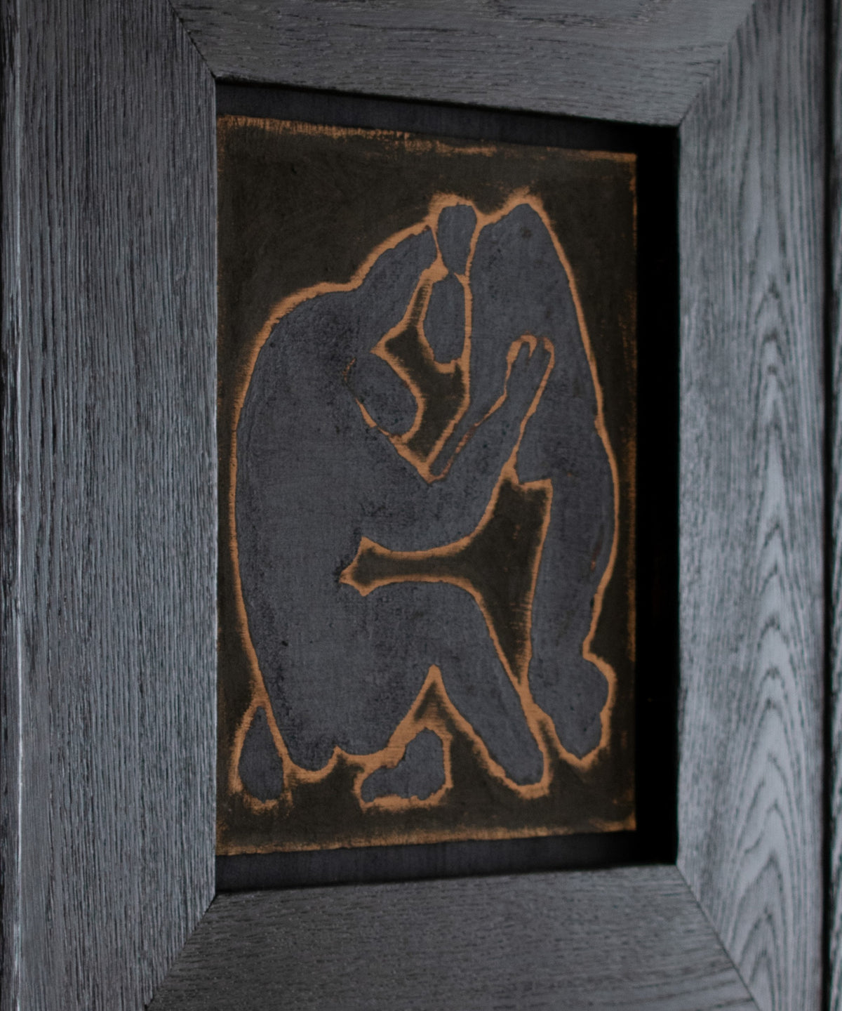 Original wall art by Marcsen featuring a dark silhouette of two embracing figures on a earthy background, set within a thick dark brown wooden frame against a light cream wall.