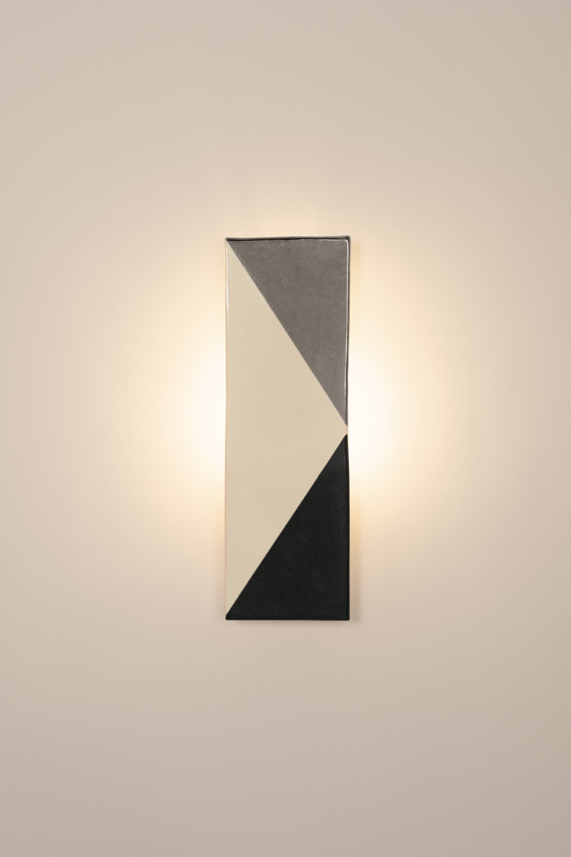 Wall-mounted light fixture by Violaine d'Harcourt with the light on. The design is a geometric pattern in grey, black and white.