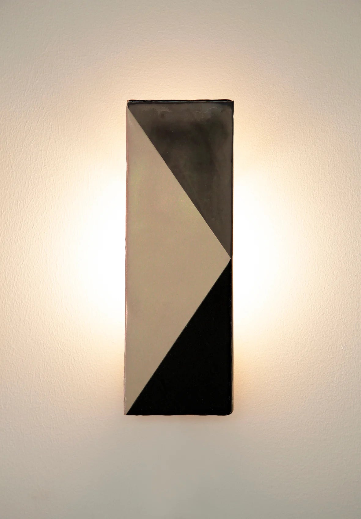 Wall-mounted light fixture by Violaine d'Harcourt with the light on. The design is a geometric pattern in grey, black and white.