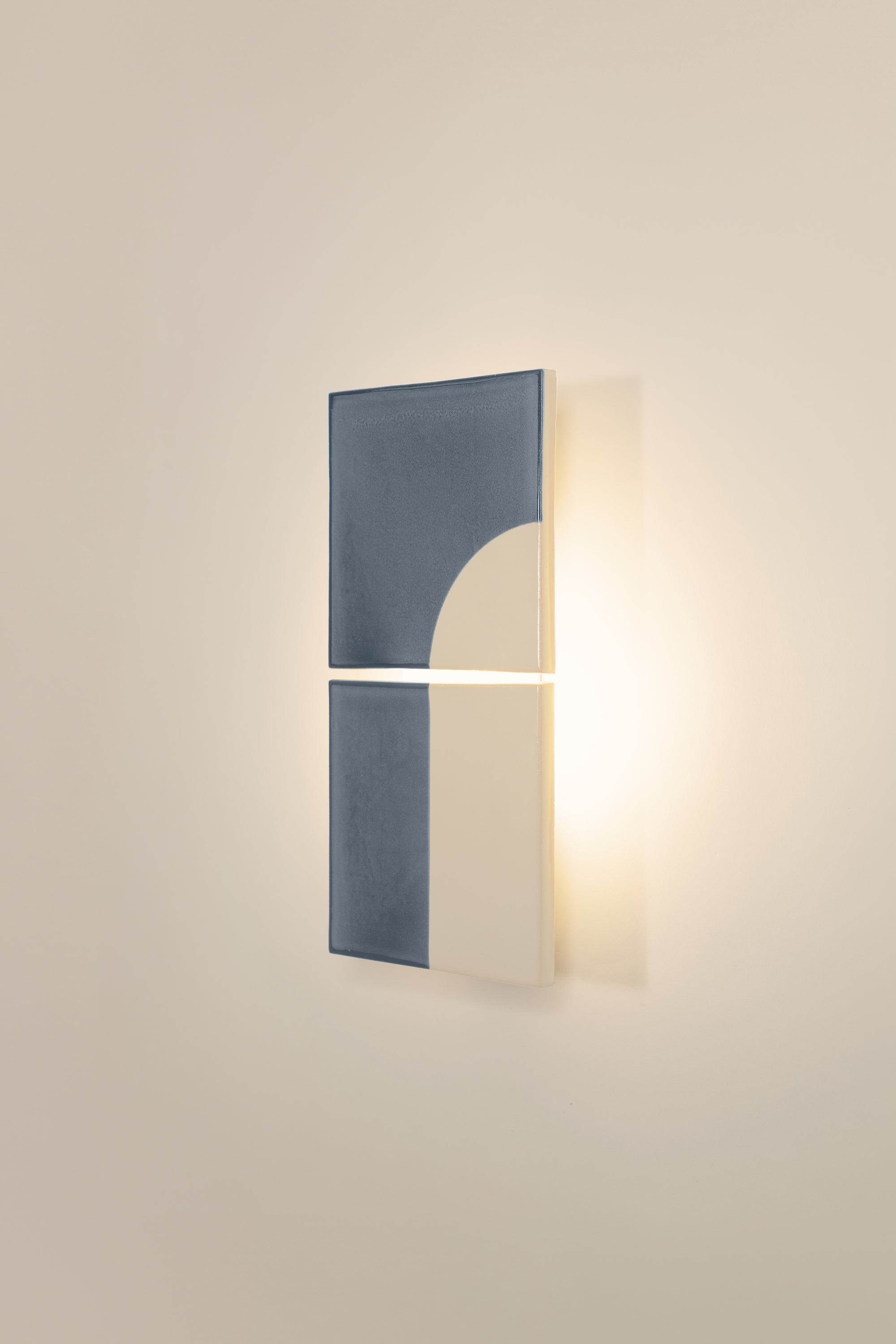 Wall-mounted light fixture by Violaine d'Harcourt with the light on. The design is a geometric pattern in blue and white with a neutral background.