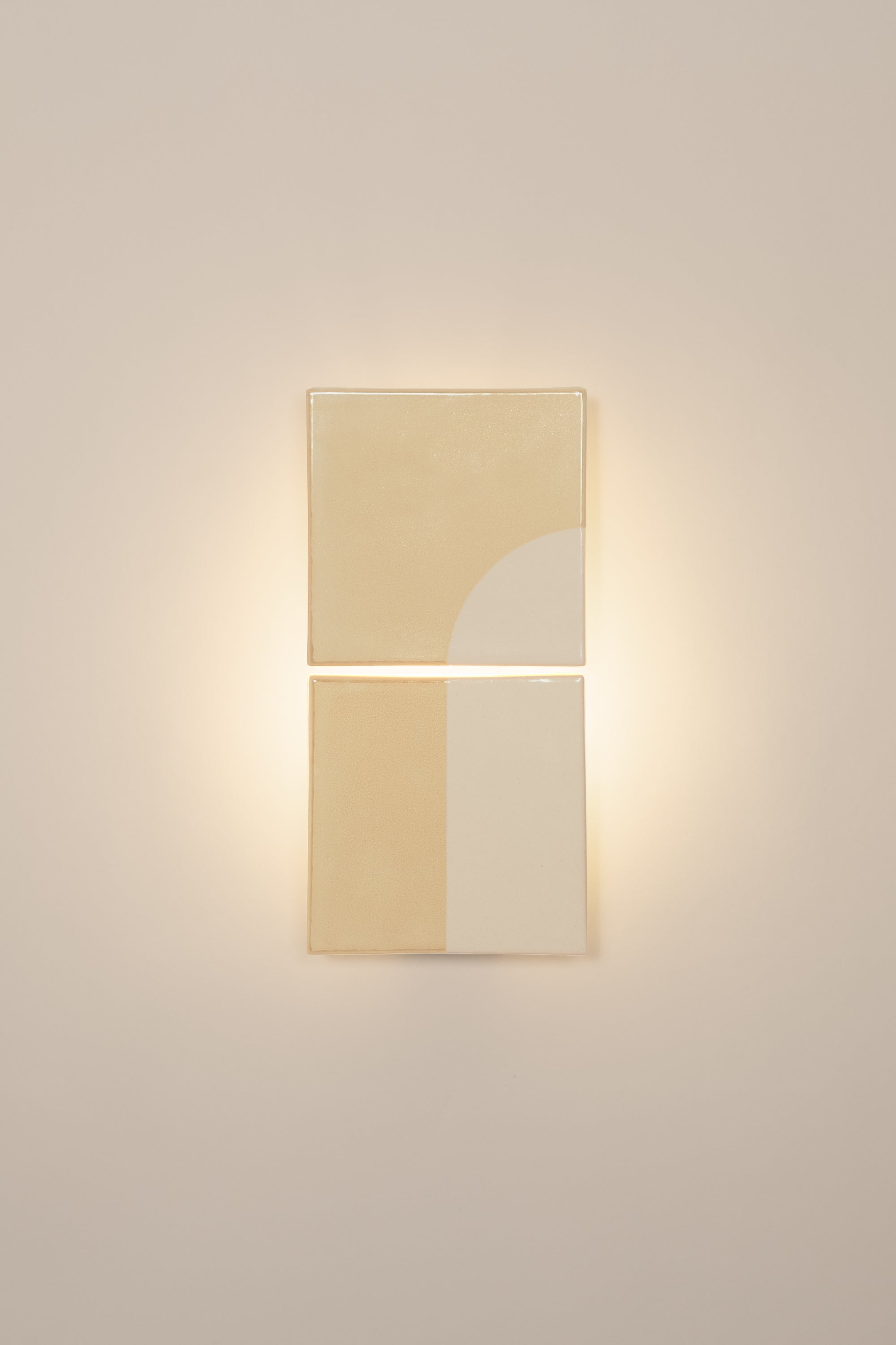 Wall-mounted light fixture by Violaine d'Harcourt with the light on. The design is a geometric pattern in cream and white with a neutral background.