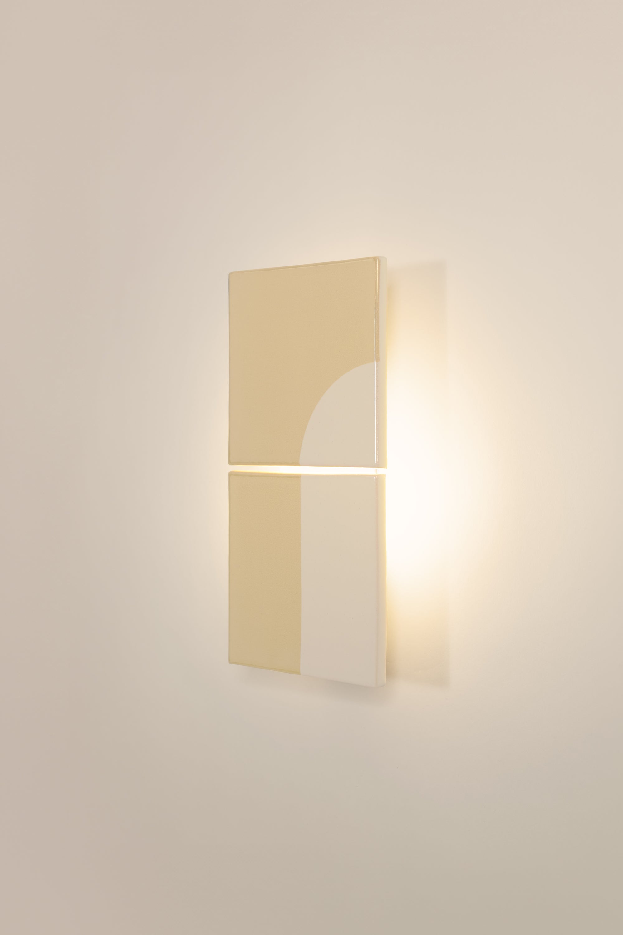 Wall-mounted light fixture by Violaine d'Harcourt with the light on. The design is a geometric pattern in cream and white with a neutral background.