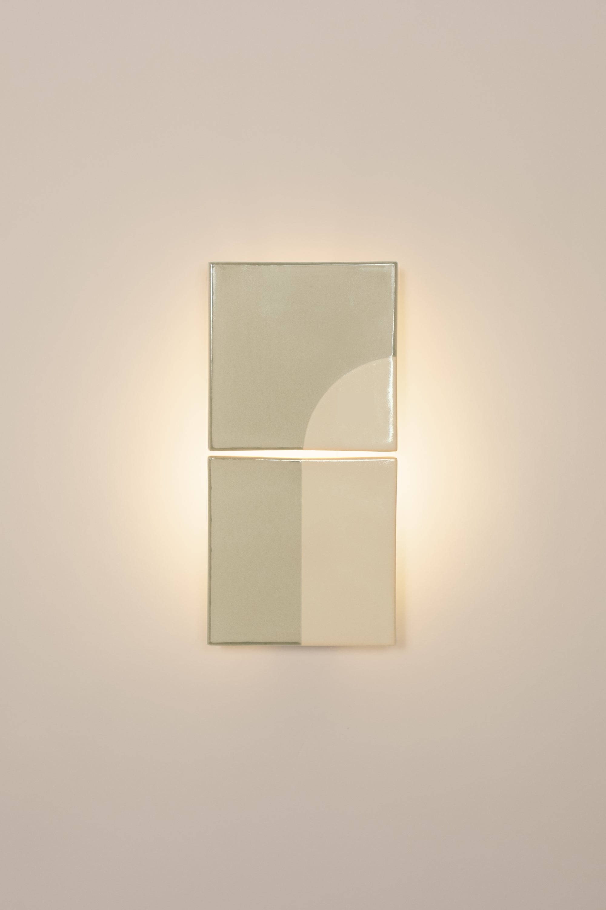 Wall-mounted light fixture by Violaine d'Harcourt with the light on. The design is a geometric pattern in green and white with a neutral background.