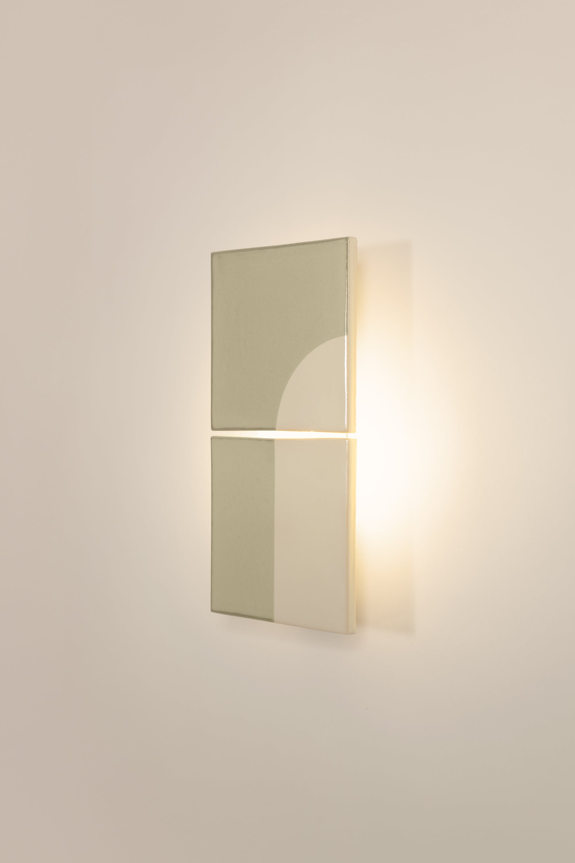 Wall-mounted light fixture by Violaine d'Harcourt with the light on. The design is a geometric pattern in green and white with a neutral background.