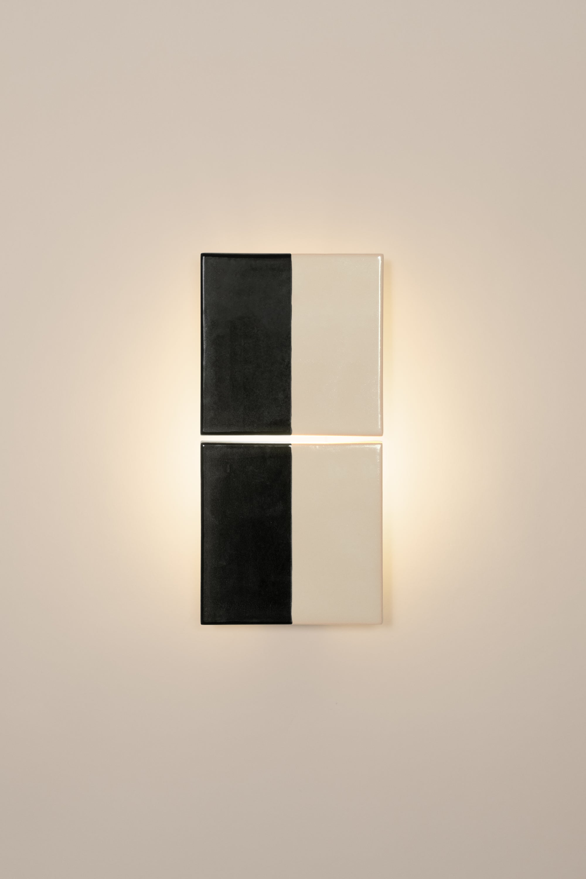 Wall-mounted light fixture by Violaine d'Harcourt with the light on. The design is two titles, half black and half white on a neutral background.