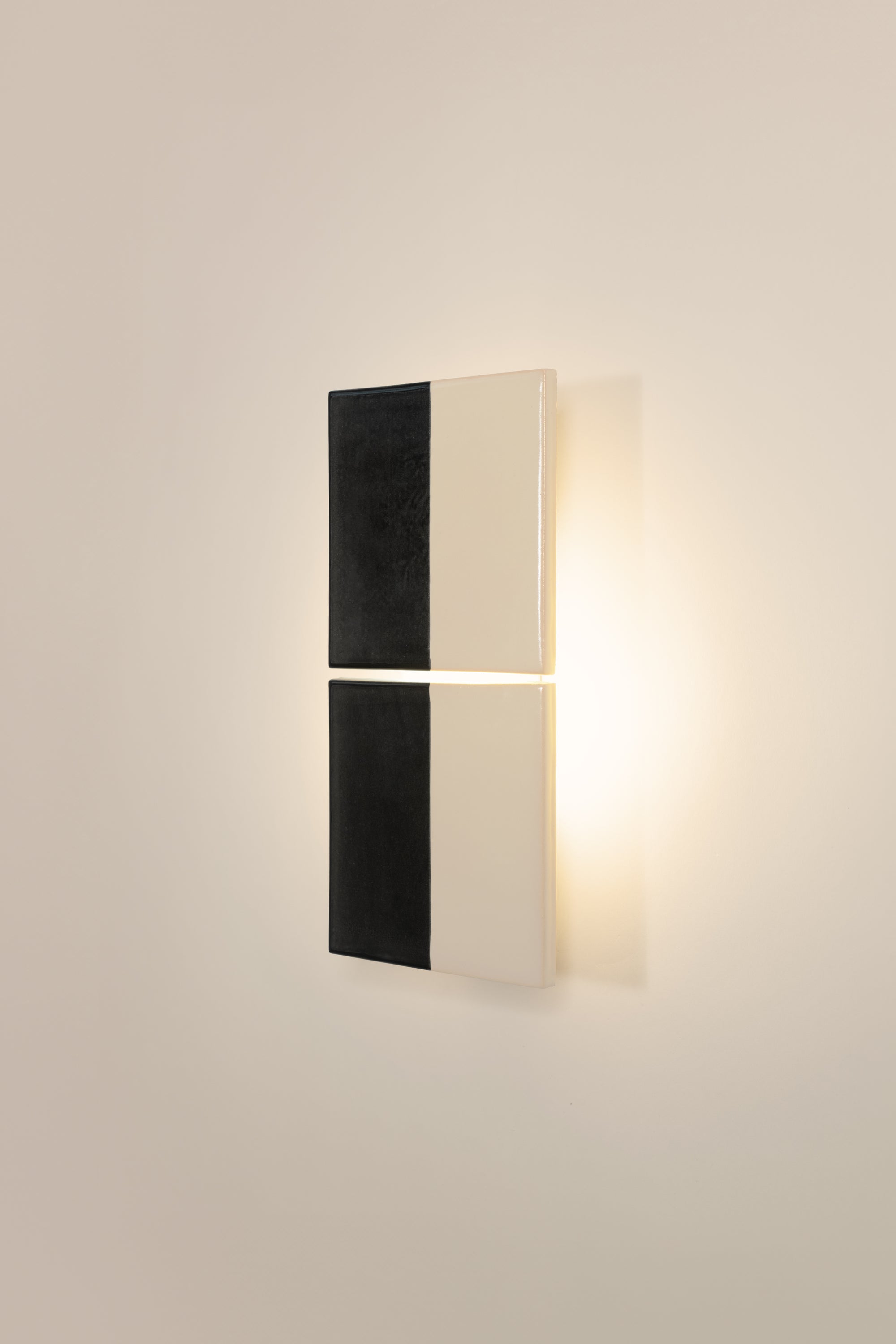Wall-mounted light fixture by Violaine d'Harcourt with the light on. The design is two titles, half black and half white on a neutral background.