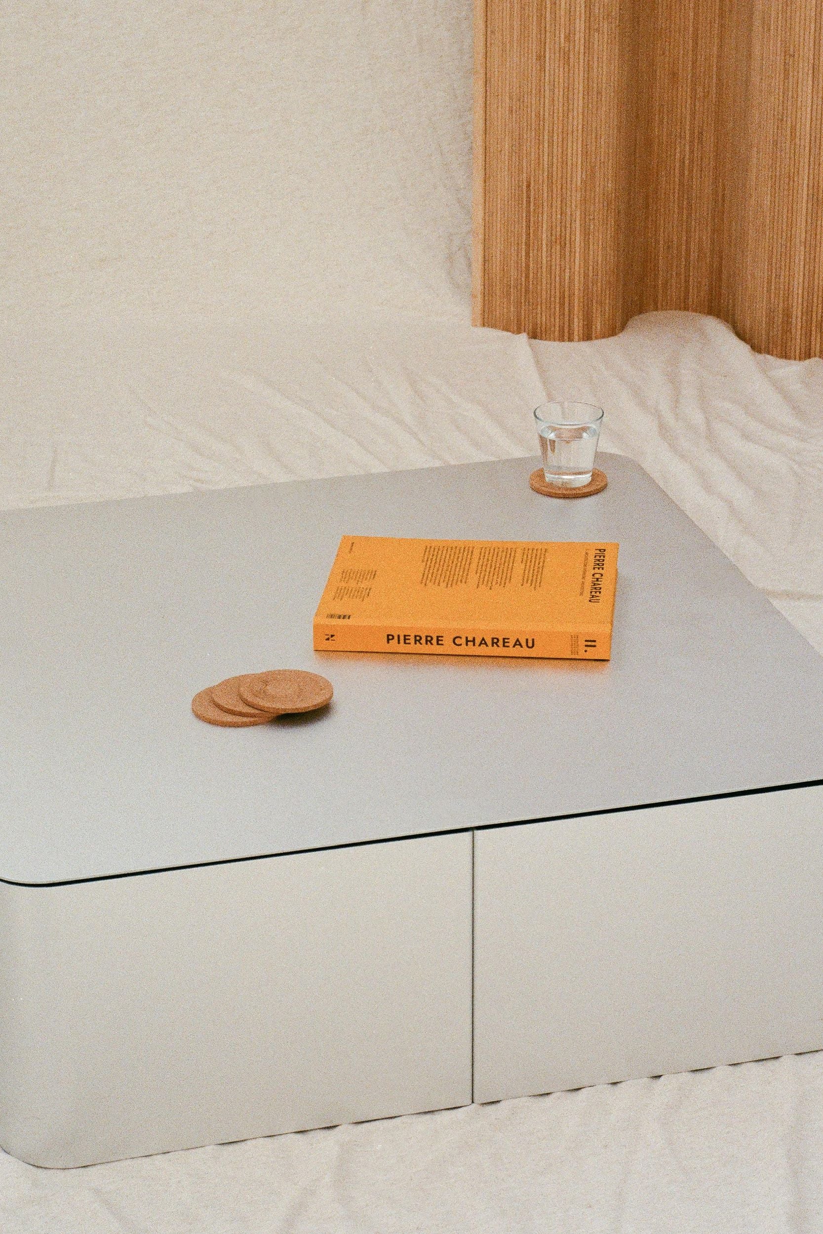 Coffee table by PARCTA. Placed on top is a glass of water, coasters and a book. The table is sat on a white cloth.