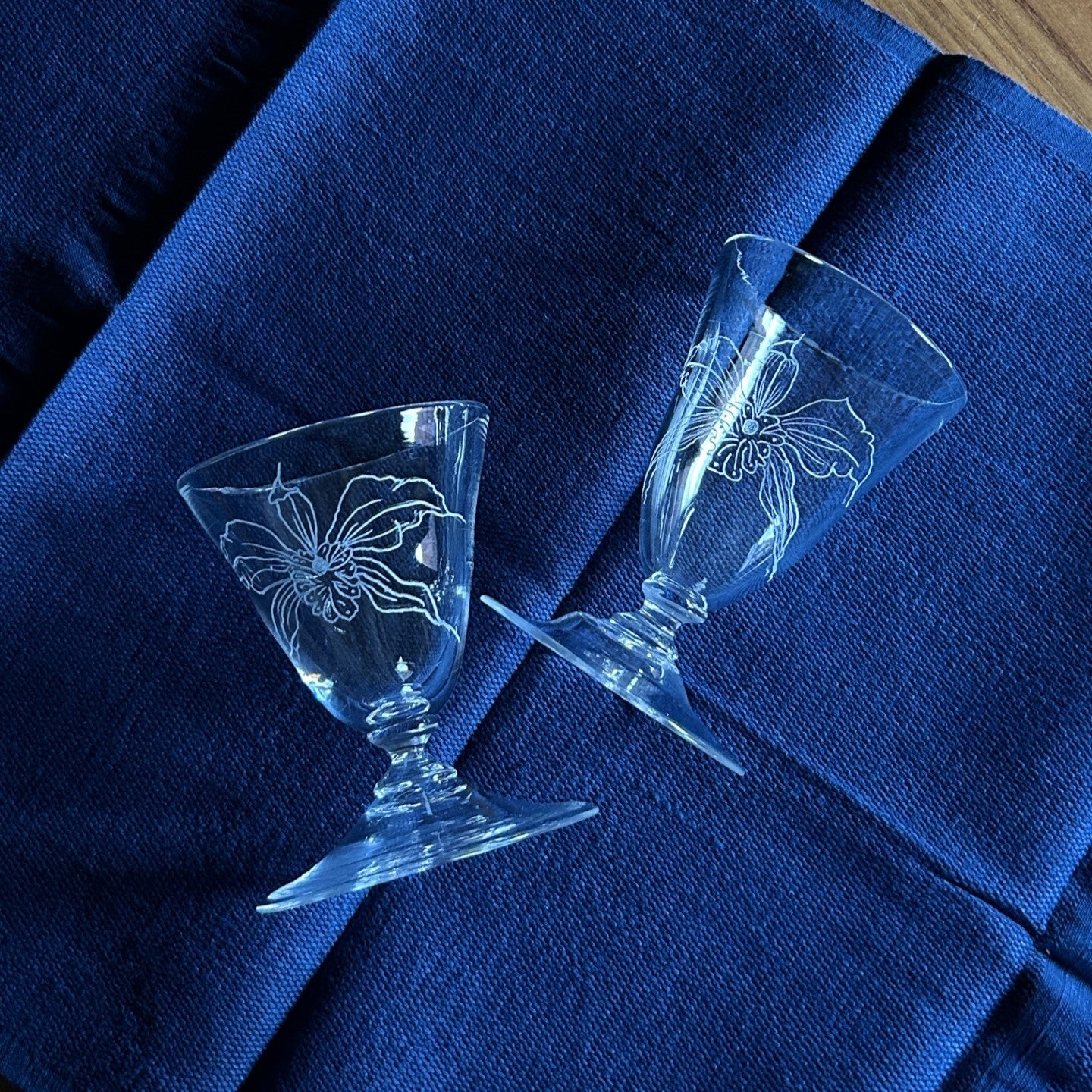 Two wine glasses with engraved flowers by Bastian Bjerge lying down on blue table linen.
